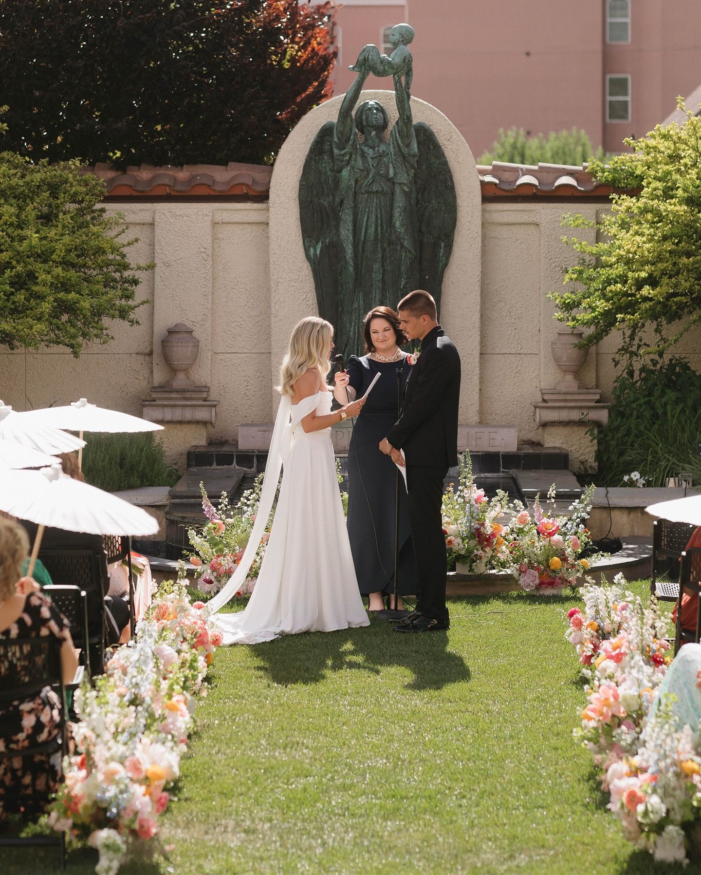 Erica officiating a garden wedding as the bride and groom exchange personal vows surrounded by family and friends