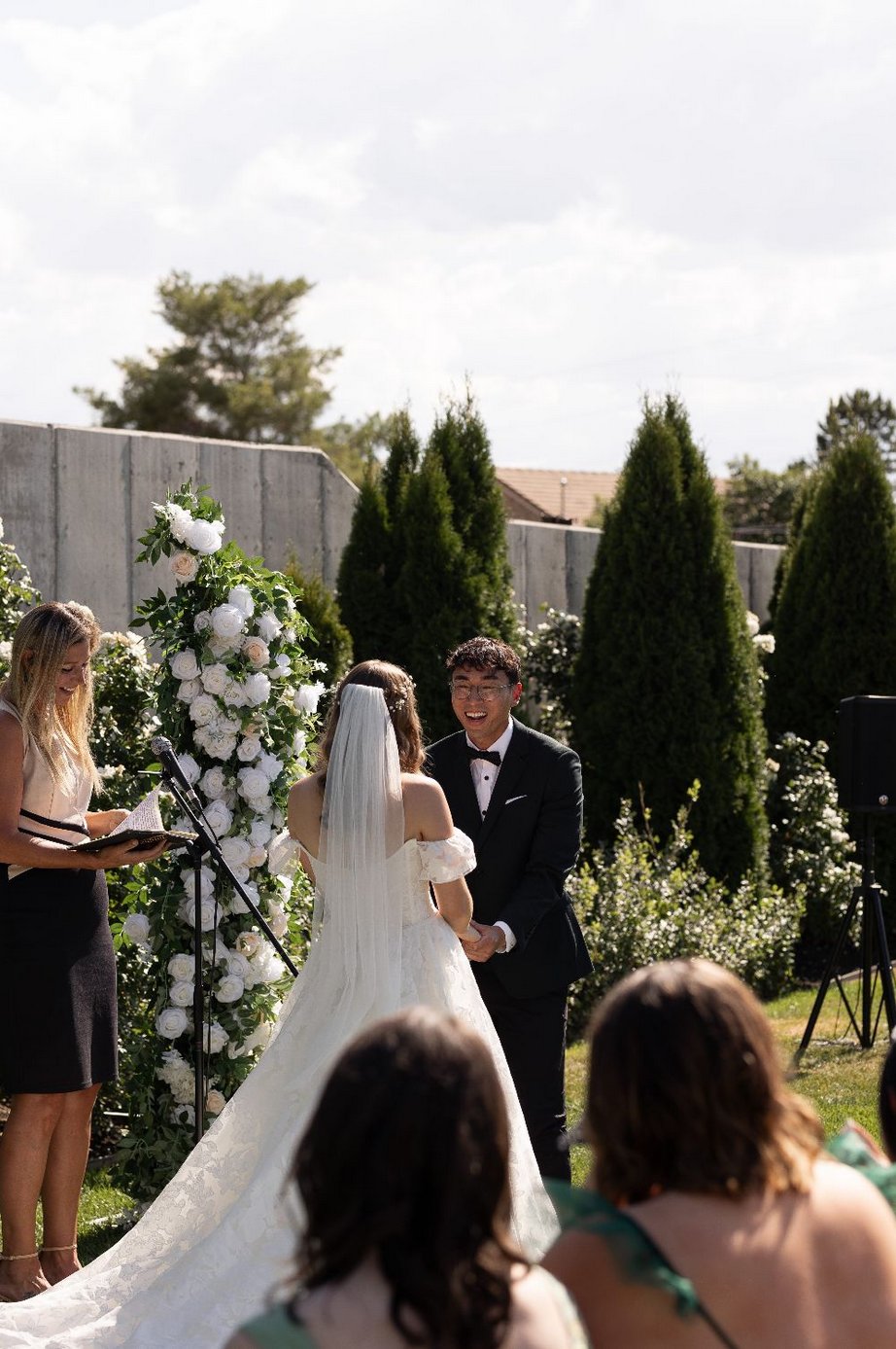 Laura officiating a backyard wedding as the bride and groom look at each other with delight