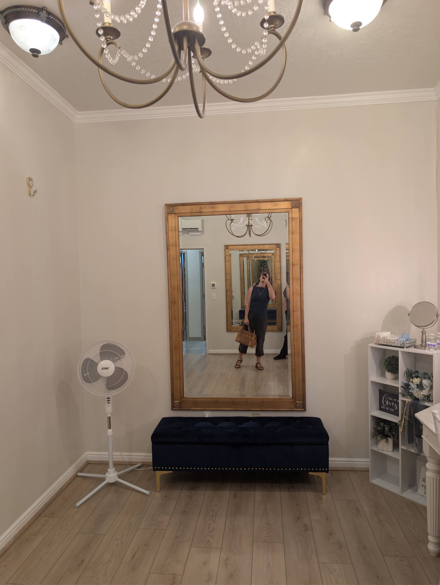 Bride's room with a large gold-framed mirror, navy tufted storage bench, and crystal-strand chandelier