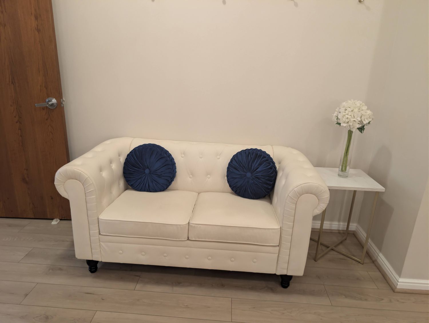 Groom's room with a cream tufted loveseat, round navy pillows, and fresh white hydrangeas on a side table