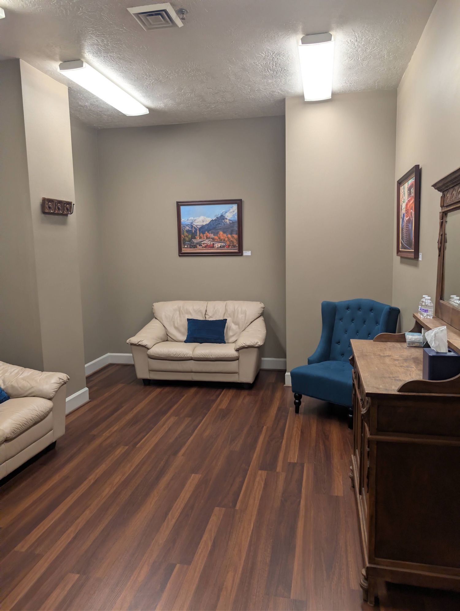 Art-filled lounge area with cream leather loveseats, a blue tufted wingback chair, and landscape paintings on the wall