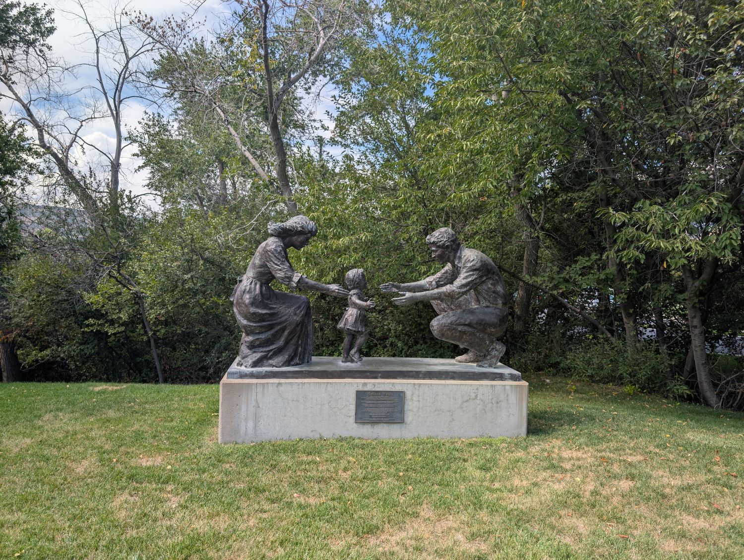 Bronze Melissa Walks statue of a small girl reaching between her kneeling mother and father, set in a grassy sculpture garden
