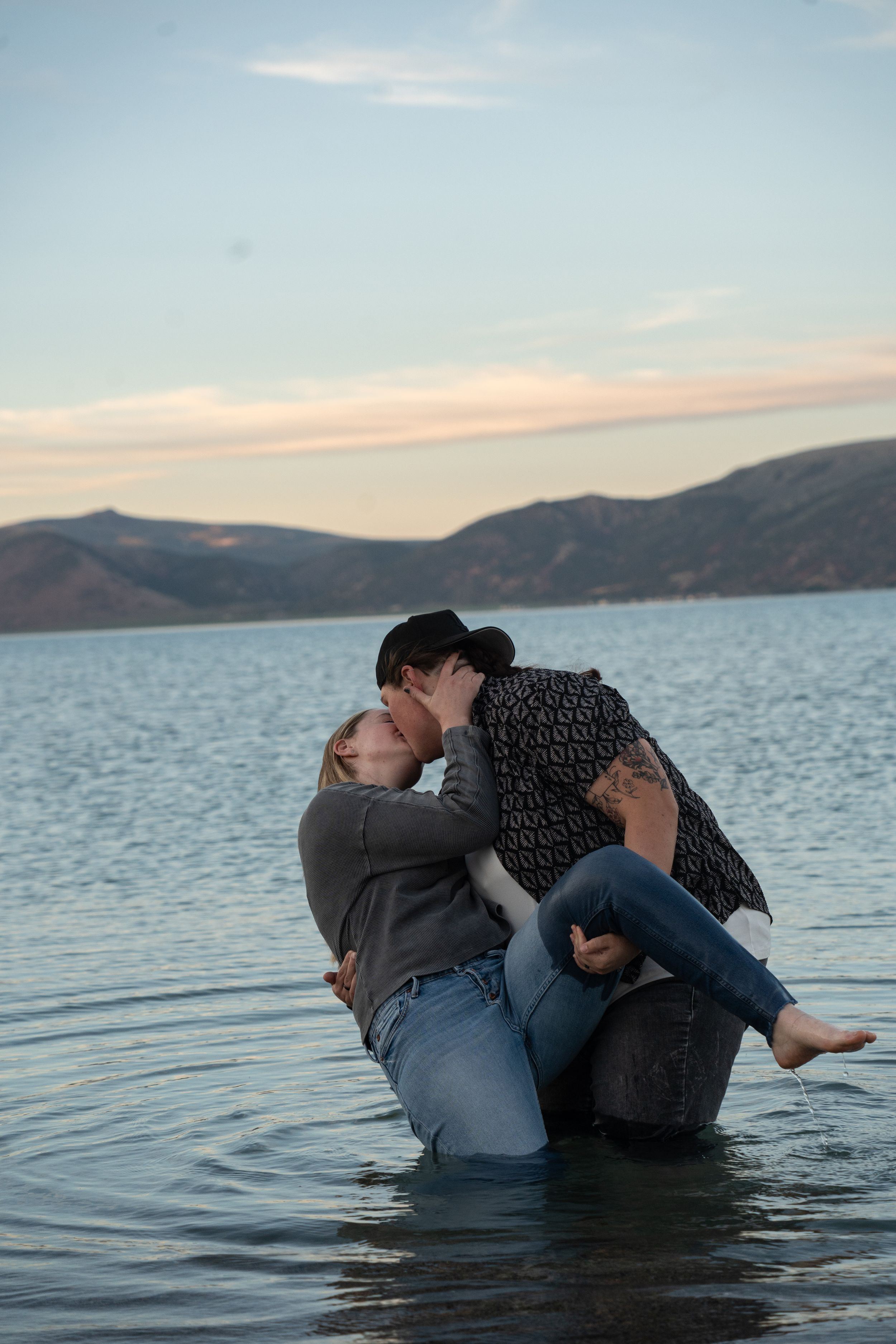 Couple kissing romantically while dip kissing in shallow bear lake water at sunset with mountain backdrop.