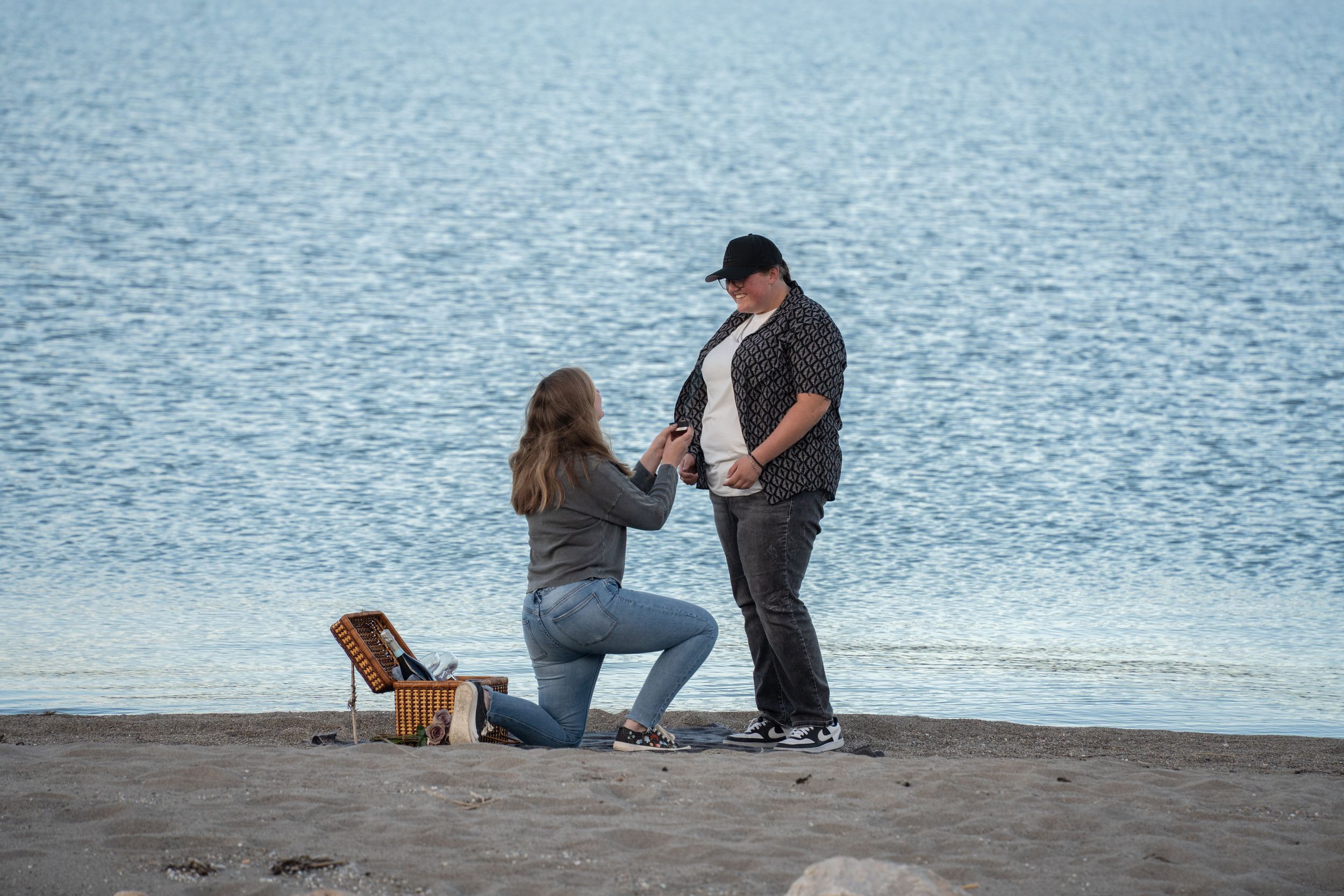 woman proposing to her girlfriend on bear lake beach with picnic basket nearby