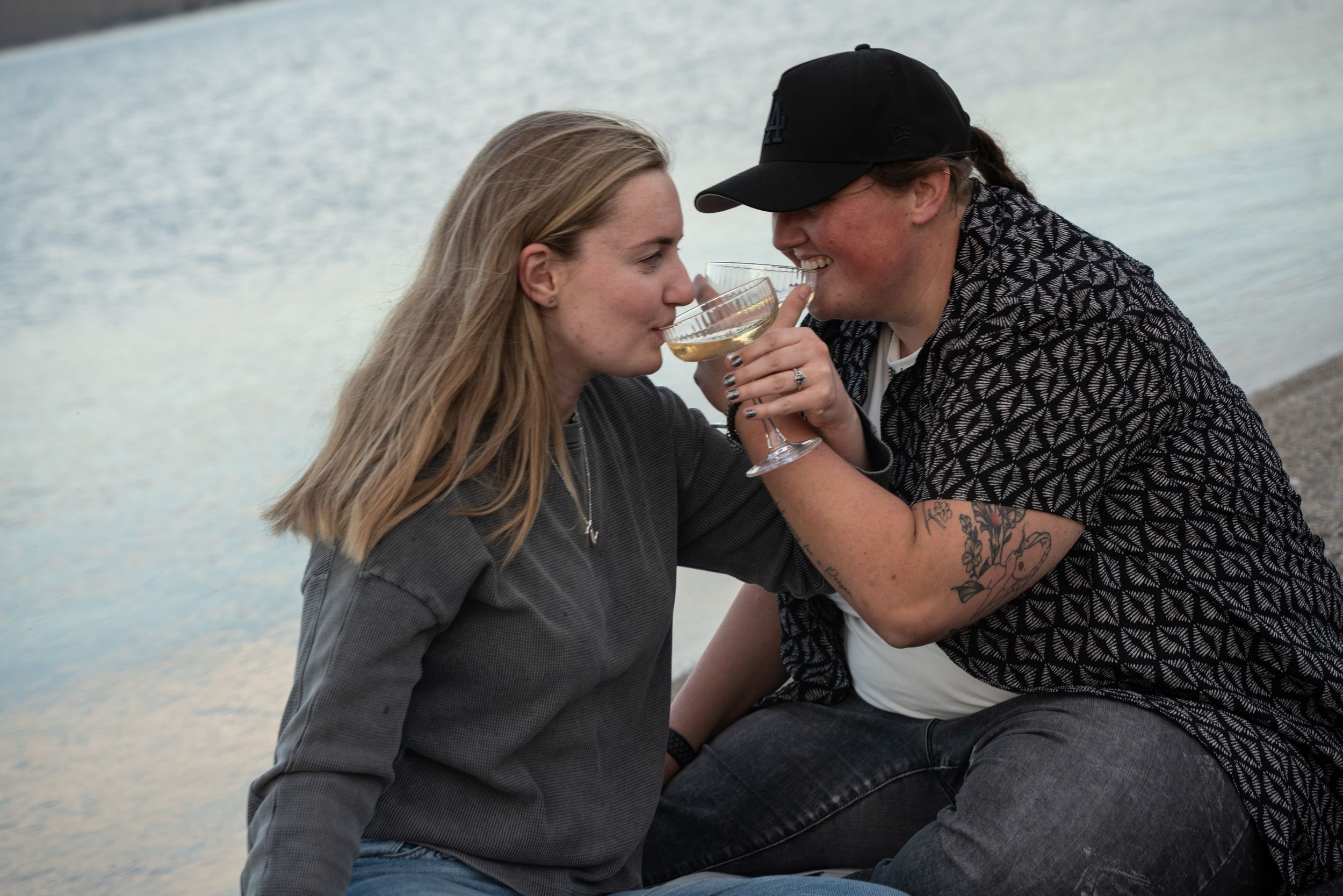 newly engaged couple sharing a glass of champagne outdoors near bear lake, sitting close together in a romantic moment.