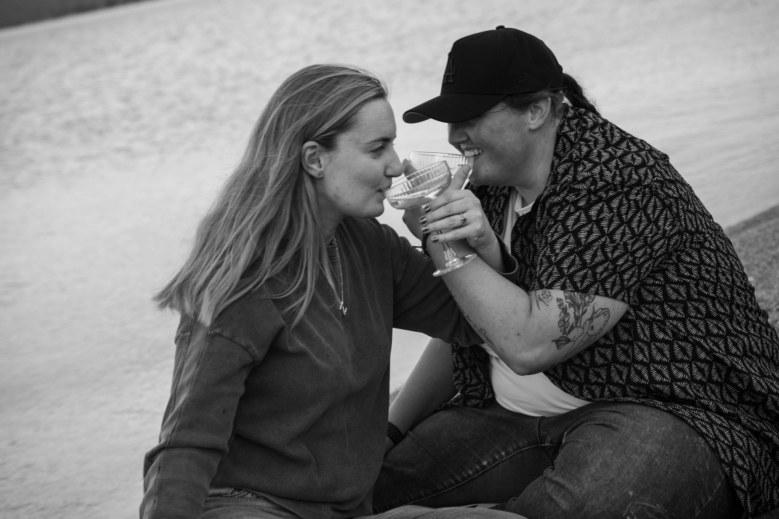 Black and white photo of a lesbian couple sharing a romantic moment, drinking champagne together sitting together on bear lake beach