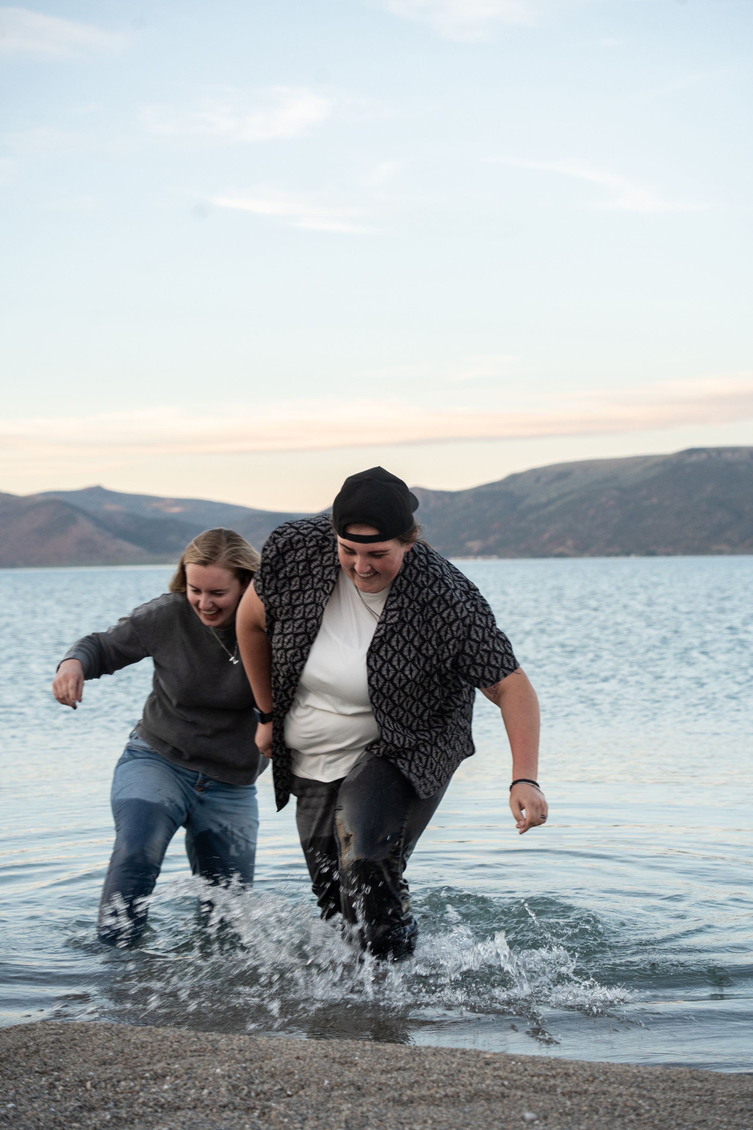 newly engaged couple running through bear lake blue water and laughing to celebrate their engagement