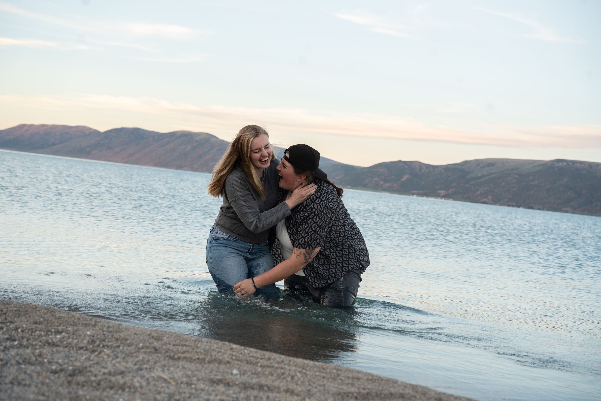 two women laughing and embracing in bear lake blue water with mountains in the background