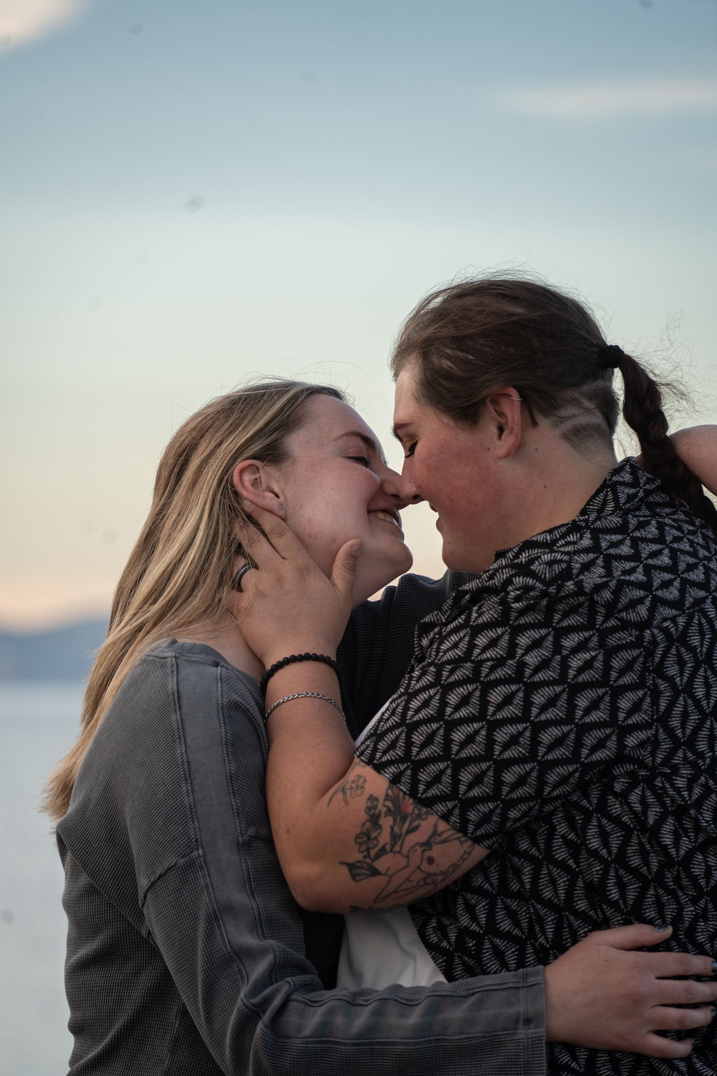 two women leaning in for an intimate kiss with an engagement ring on one left hand and bear lake in the background