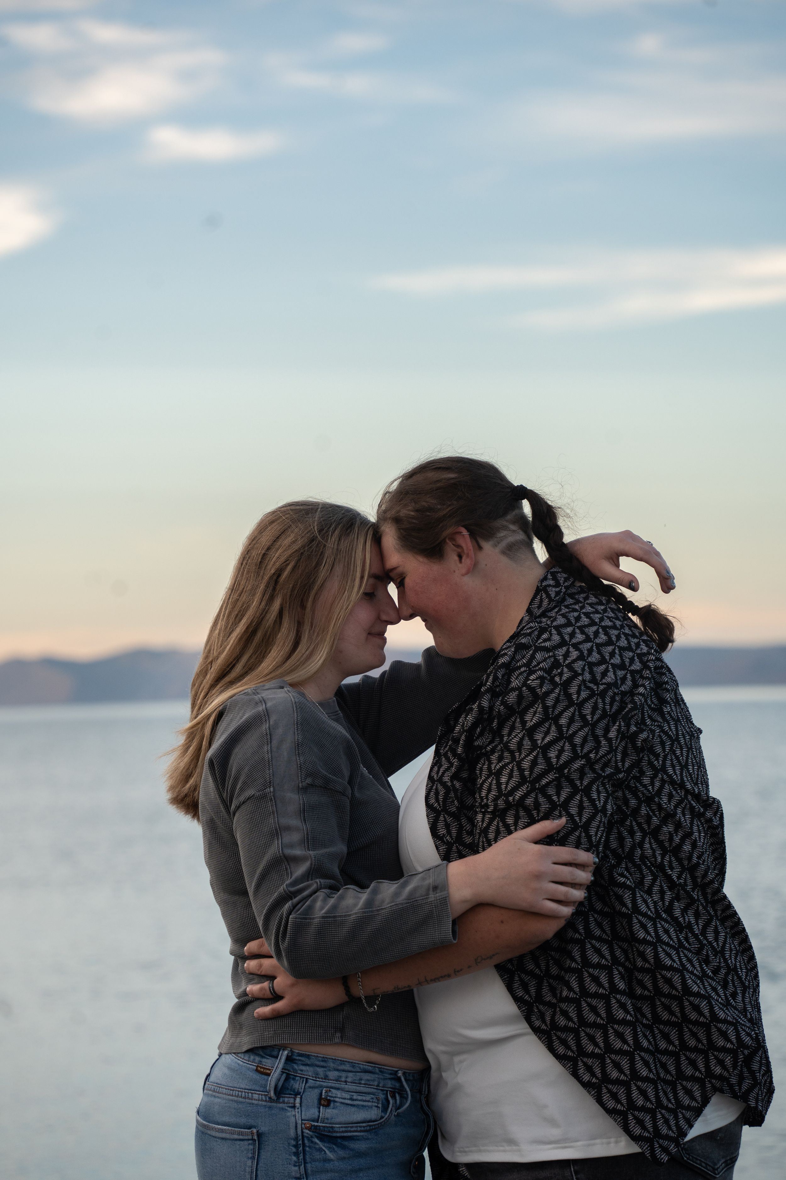 Romantic couple embracing and touching foreheads at sunset by a calm bear lake with mountains in the background.