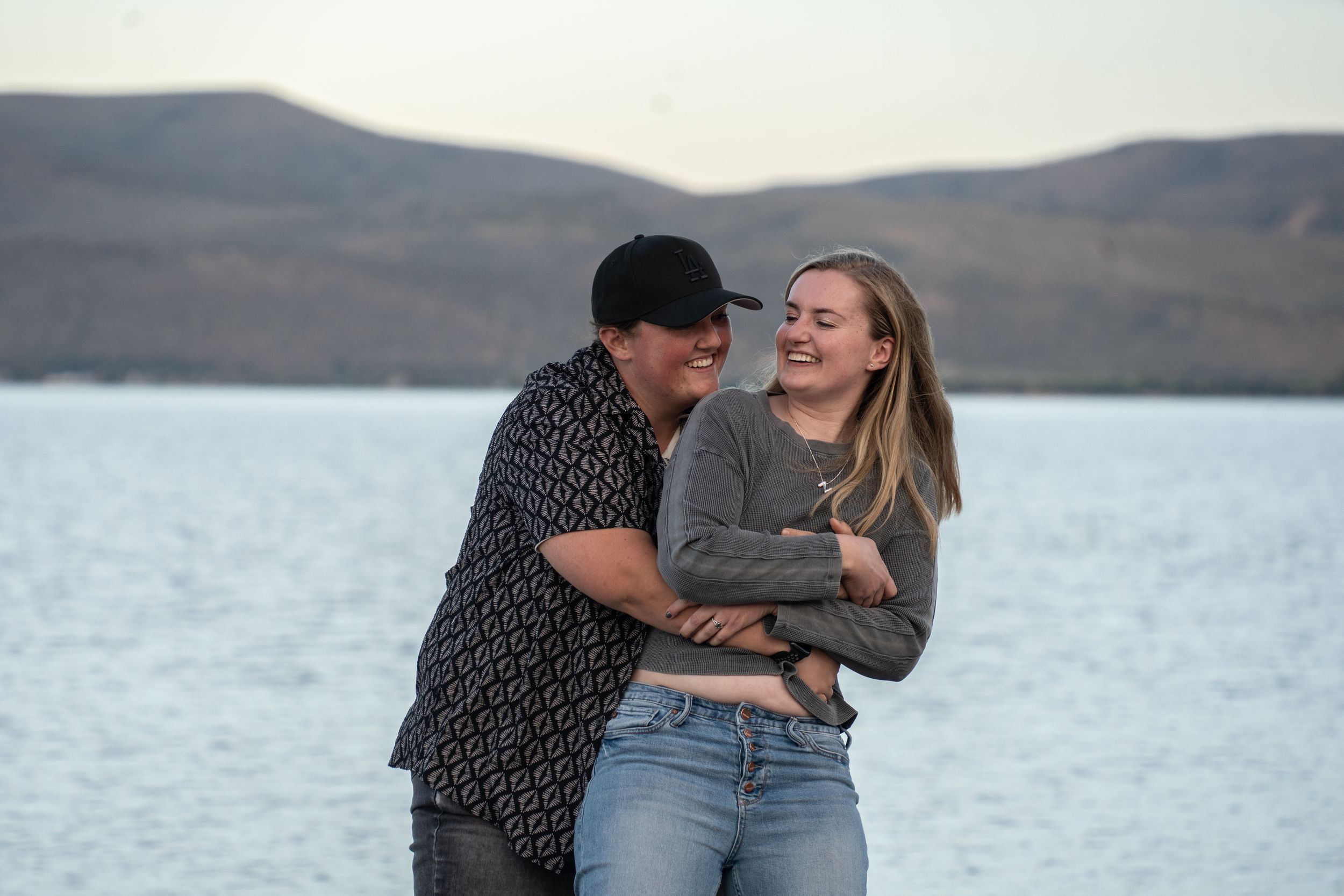 wlw Couple laughing and embracing by bear lake with mountain views in the background.