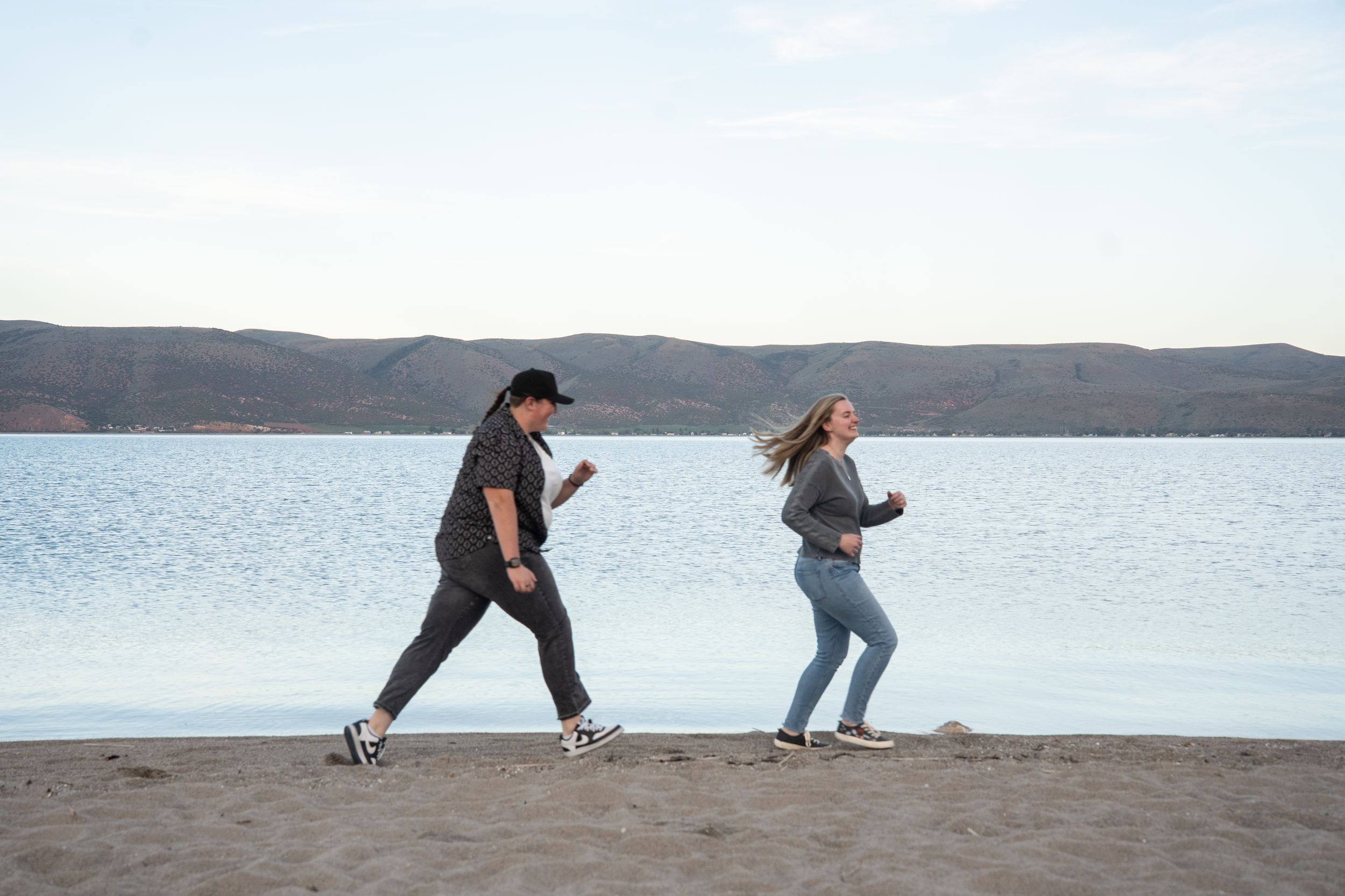 woman chasing her fiance along bear lake shoreline with mountains in background