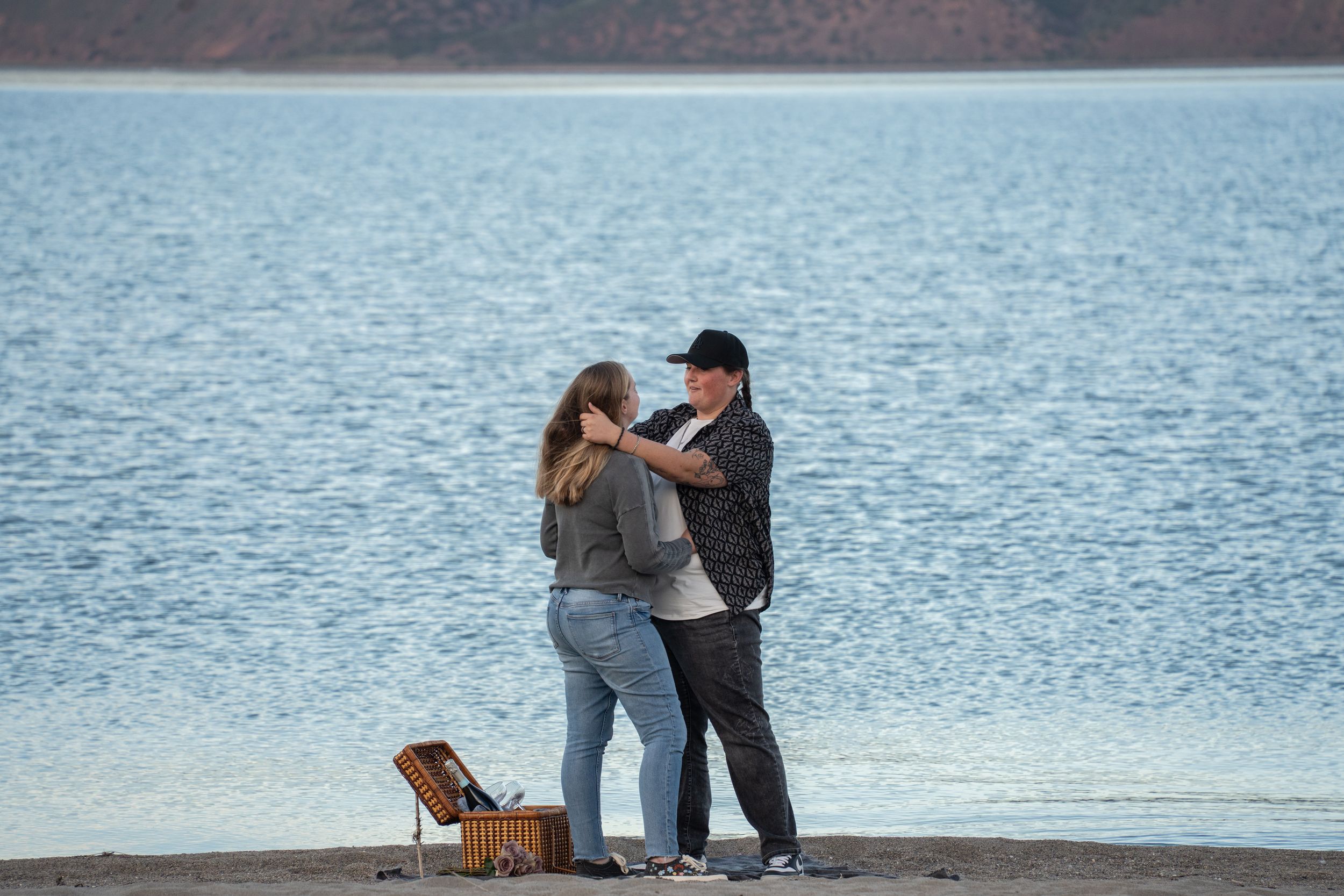 Couple sharing a romantic moment by a serene bear lake shore with a picnic basket nearby.