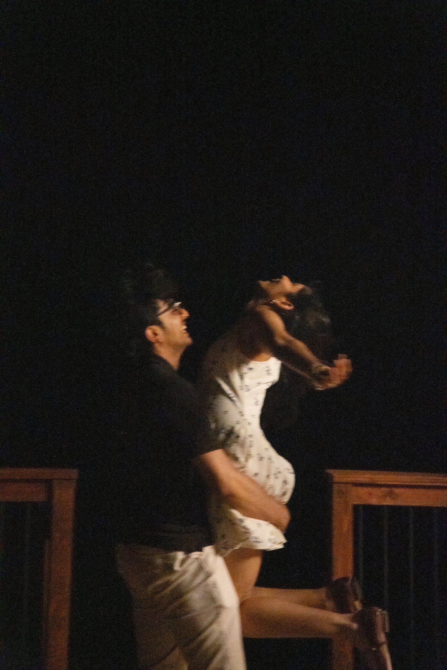 Man lifting his newly engaged partner in a celebratory spin on a wooden deck at night after his surprise proposal