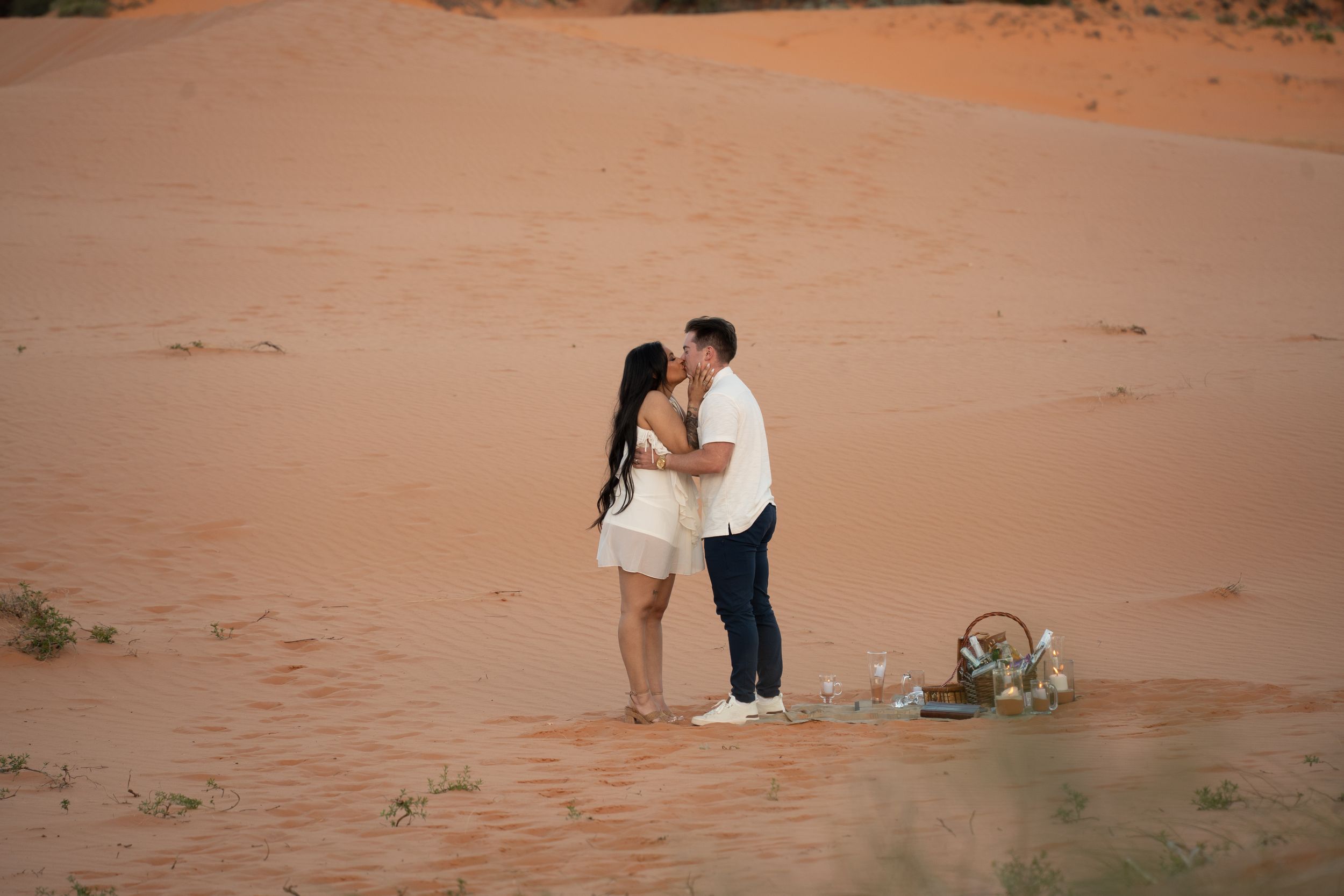 Couple sharing a romantic kiss on red sand dunes following their proposal at coral pink sand dunes