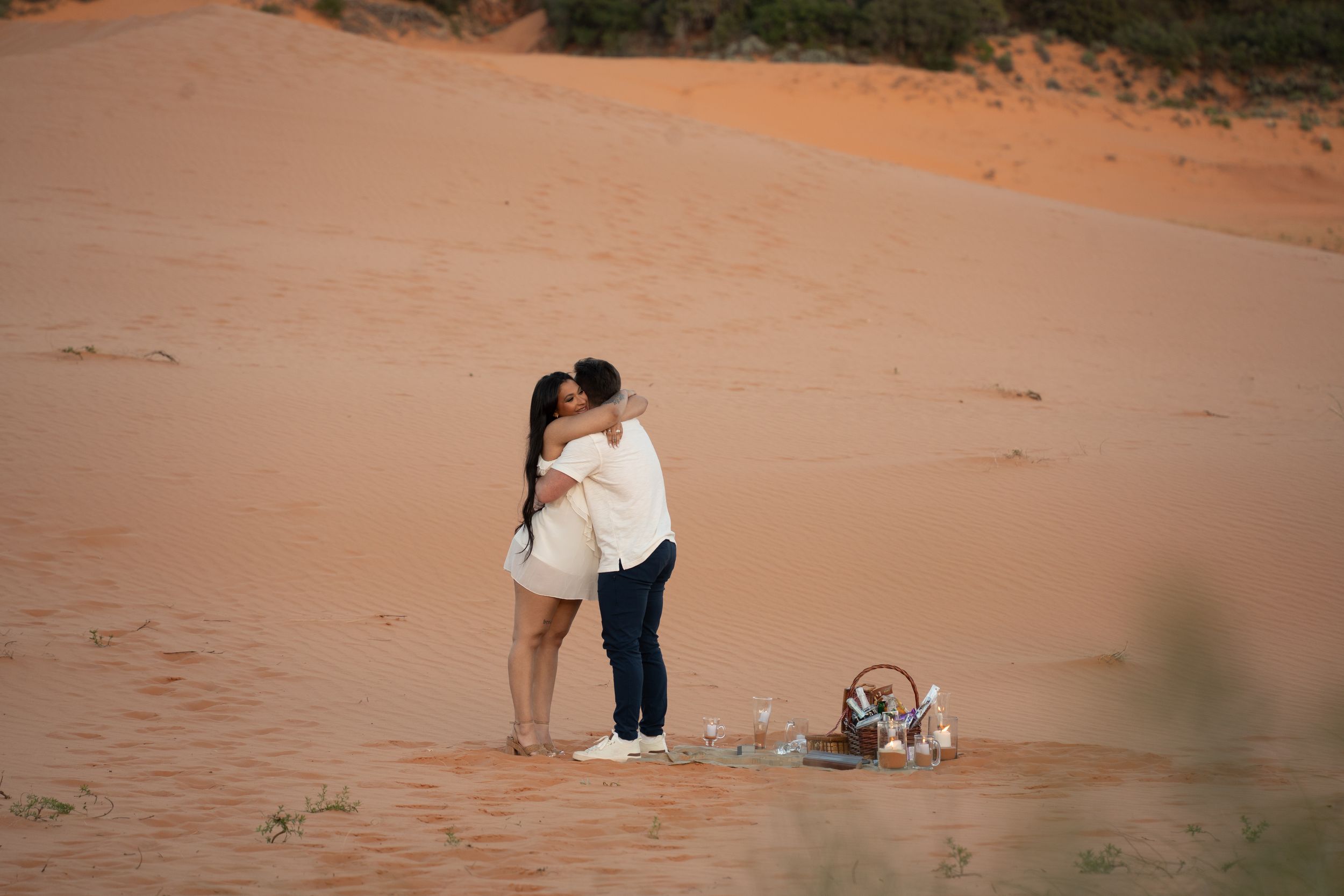 Couple sharing a romantic kiss on kanab coral pink sand dunes with a picnic basket nearby.