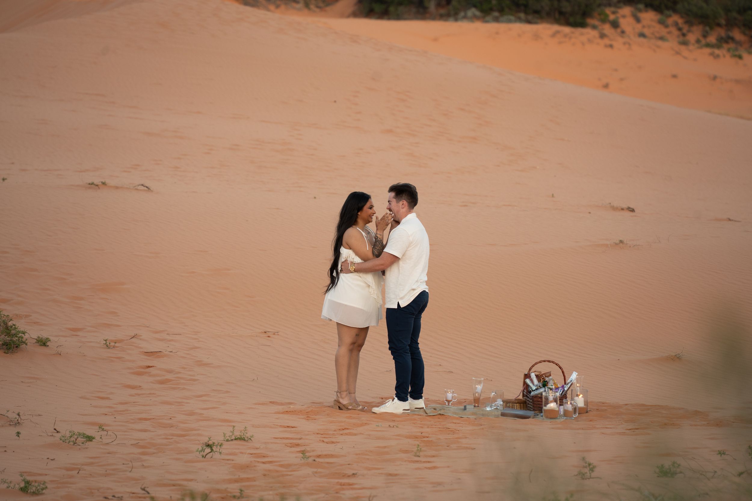 Romantic couple sharing an intimate moment on red sand dunes during a desert picnic at golden hour.