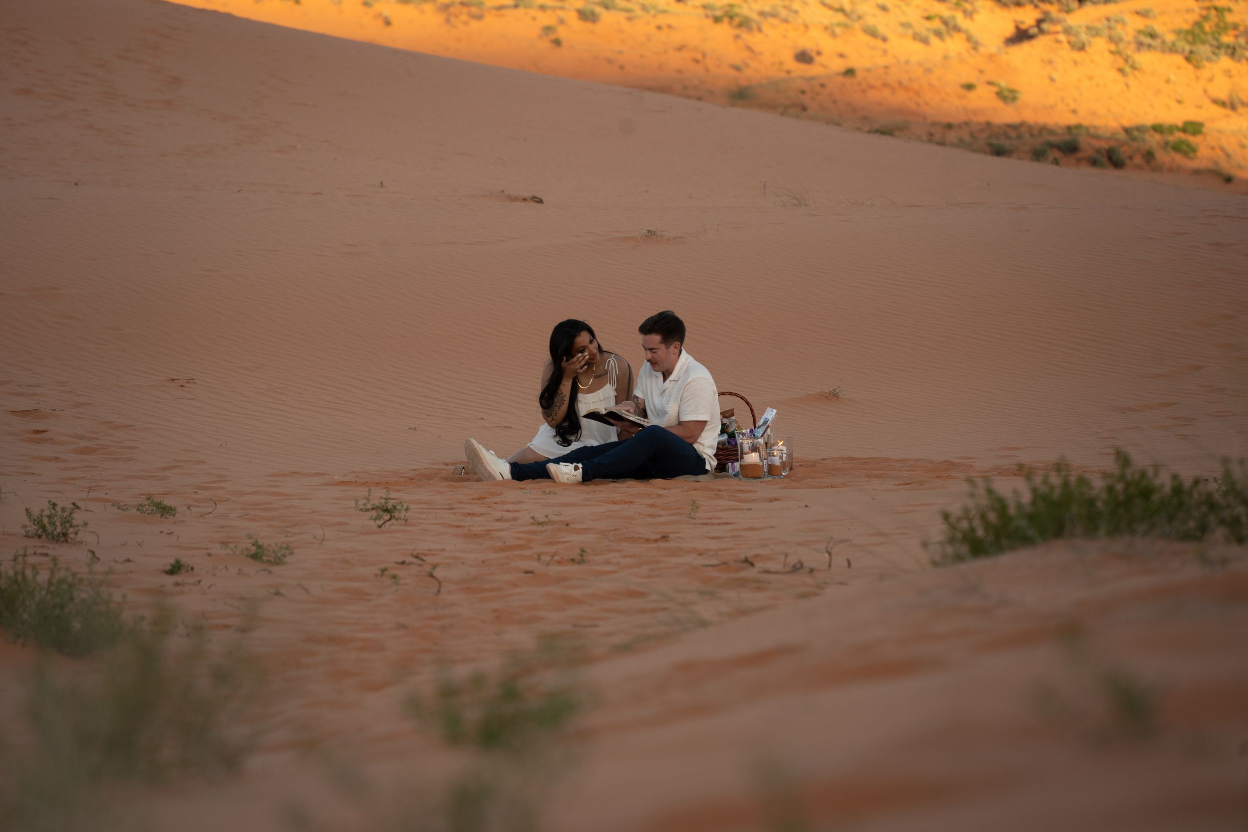 Couple sitting together on pink sand dunes at sunset in a desert landscape for a romantic picnic.