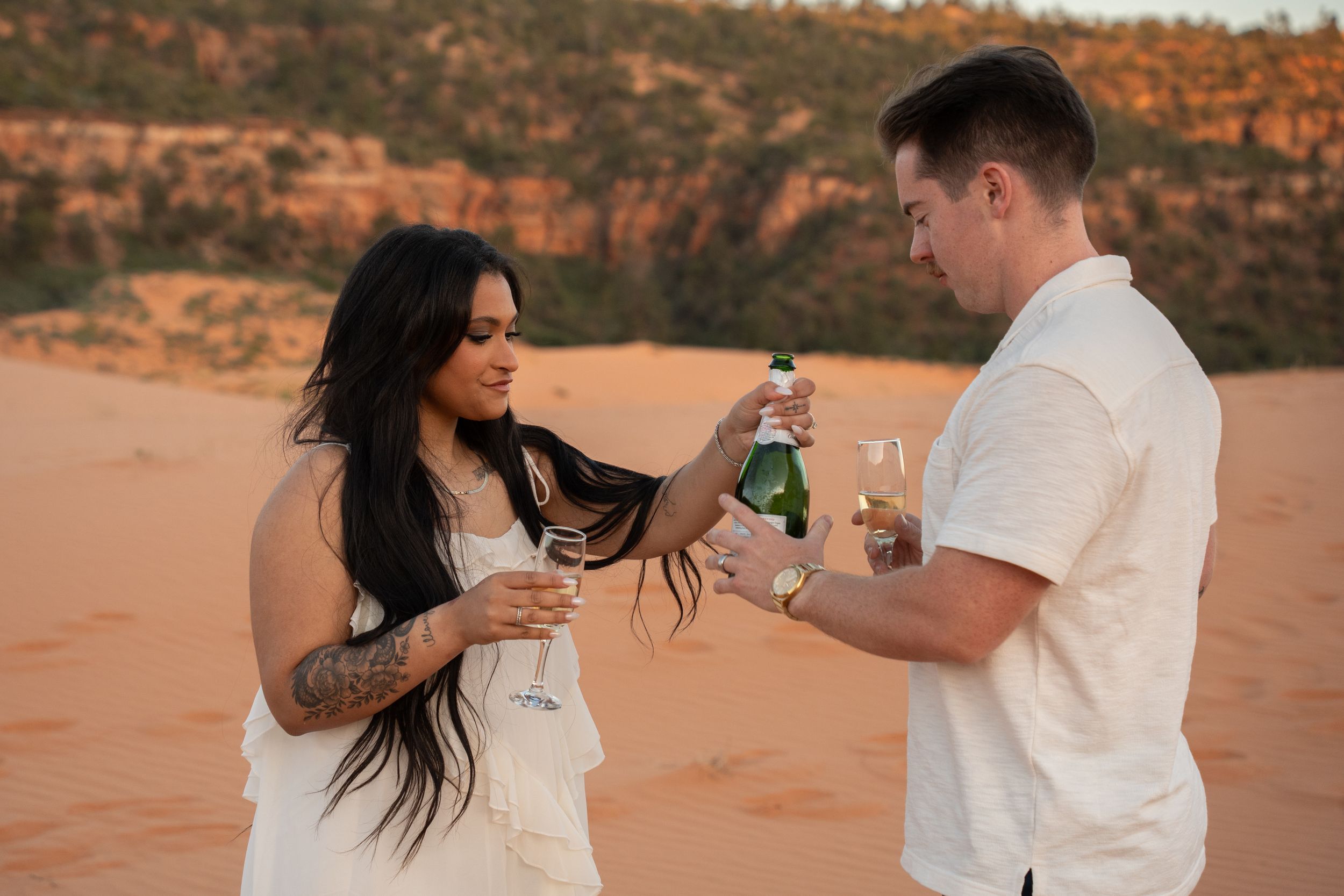 woman pouring celebratory champagne for her boyfriend to celebrate their engagement at the coral pink sand dunes