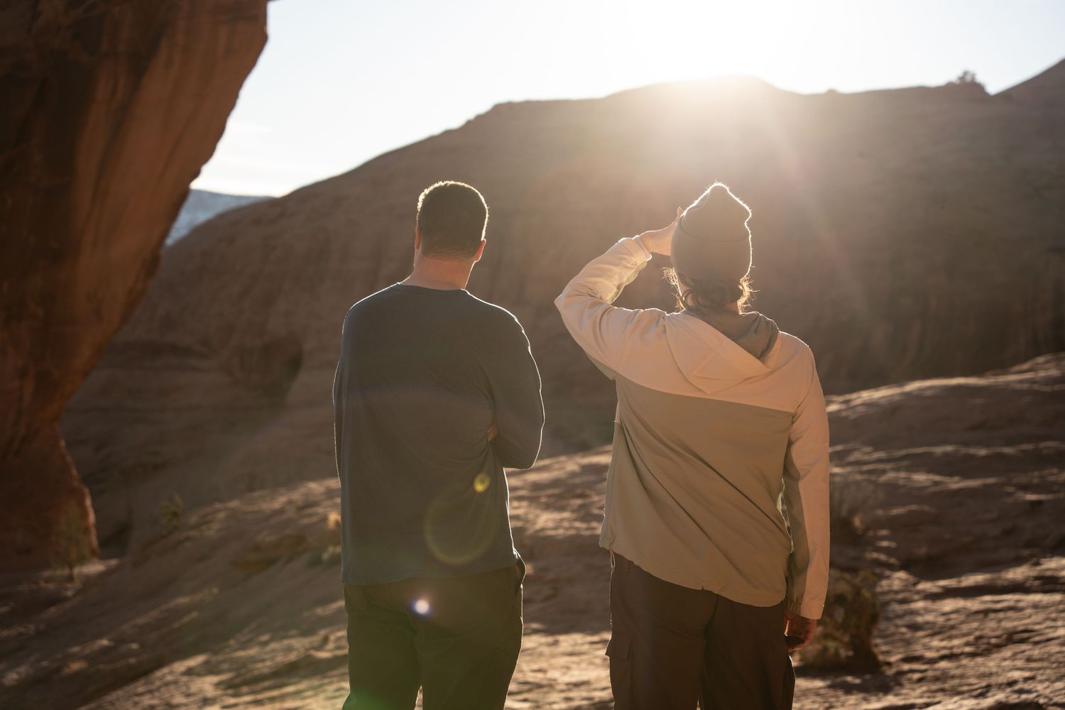 Two hikers stand facing a dramatic desert canyon landscape