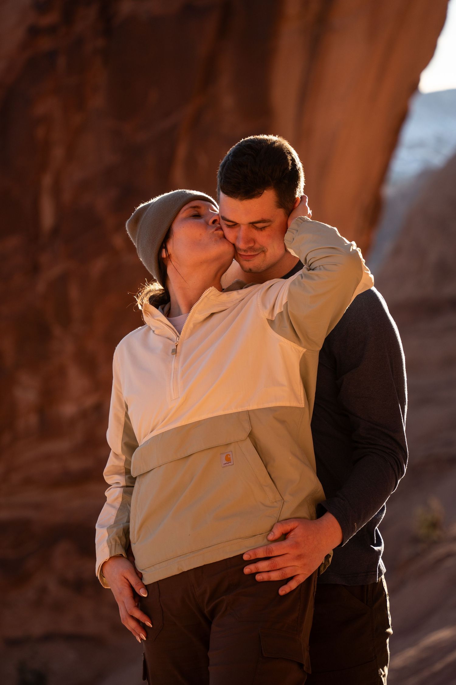 Couple sharing a romantic kiss outdoors near a red rock cliff