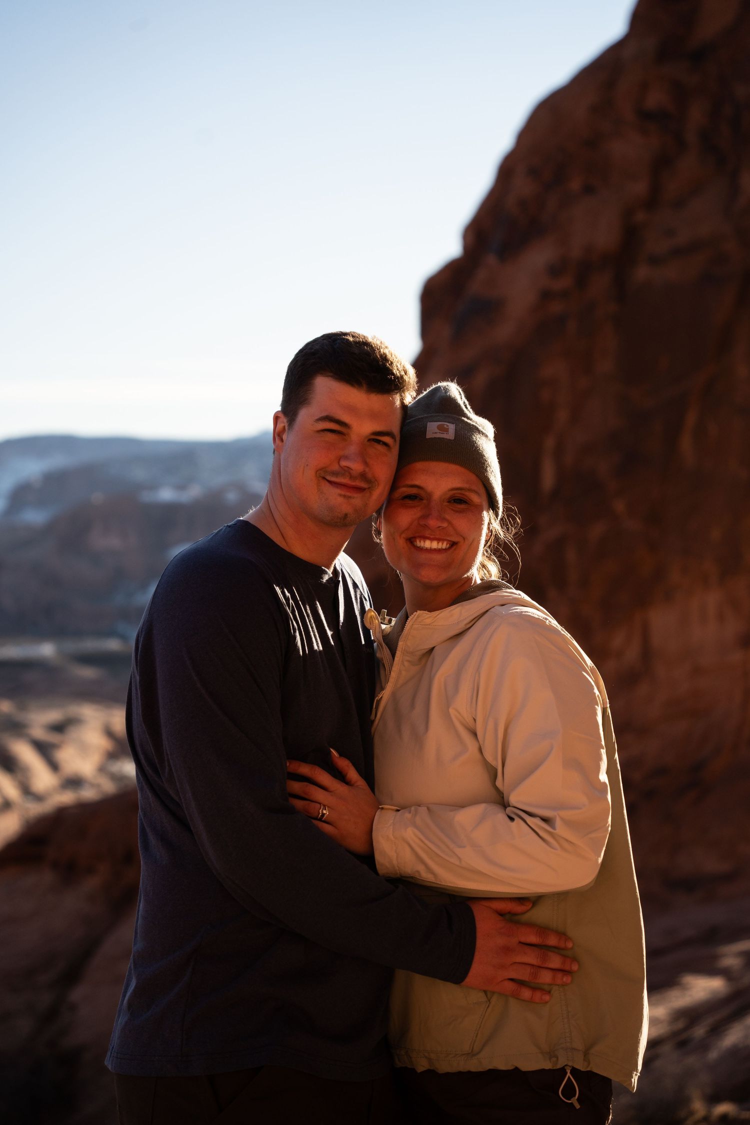 A couple embraces and smiles at a scenic desert canyon overlook