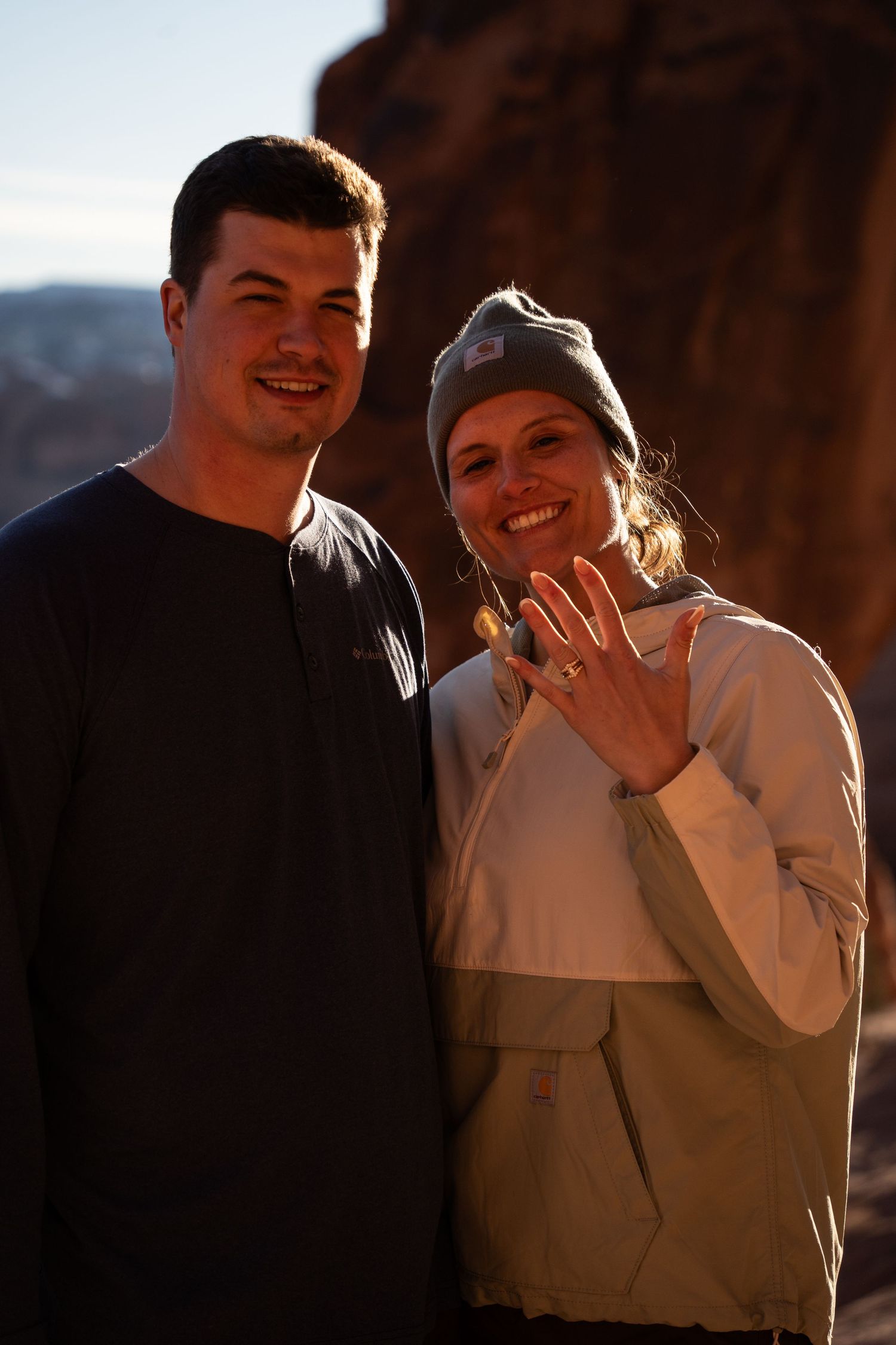 Happy couple smiling outdoors showing off engagement ring