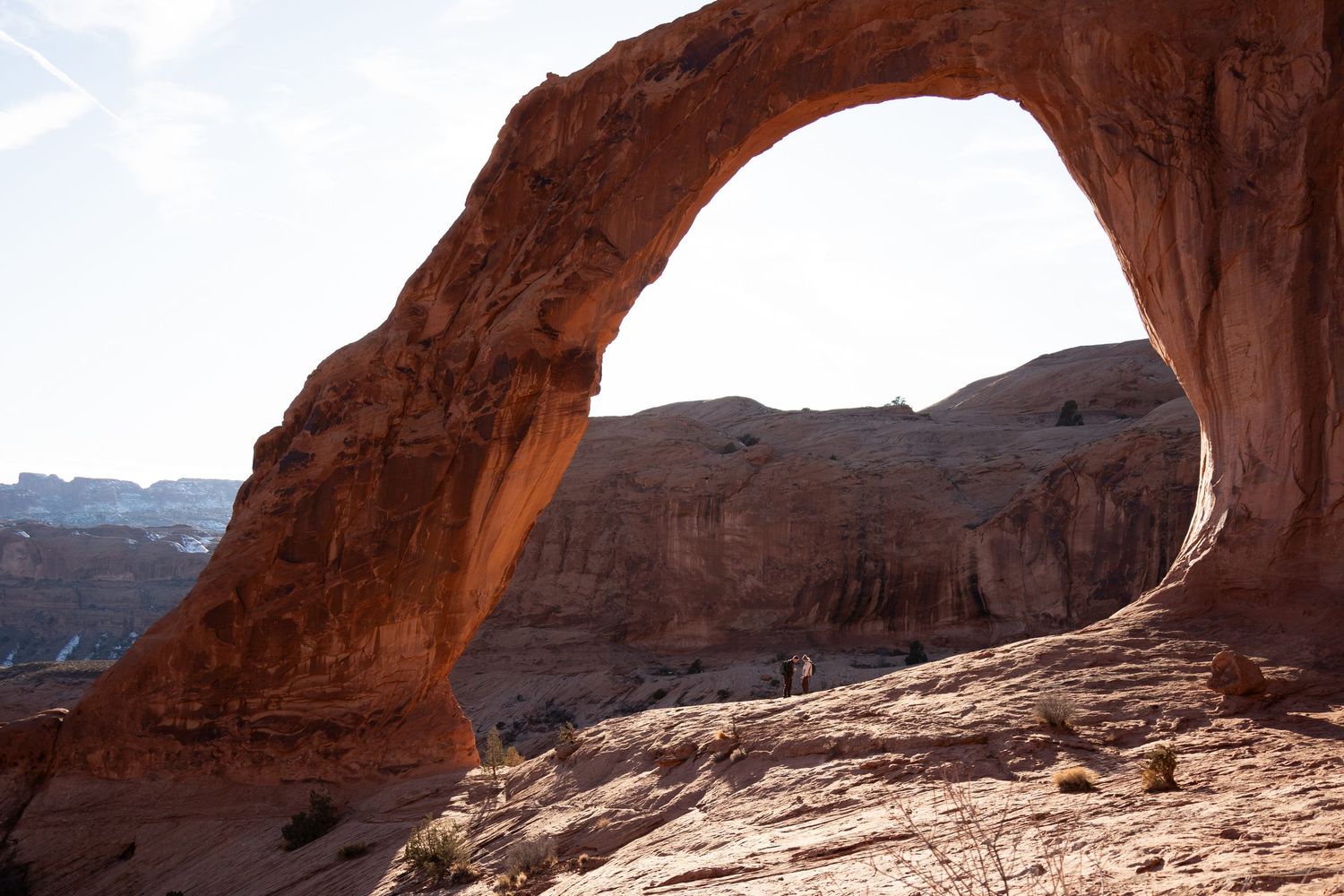 Newly engaged couple walking hand in hand away from Corona Arch at sunset