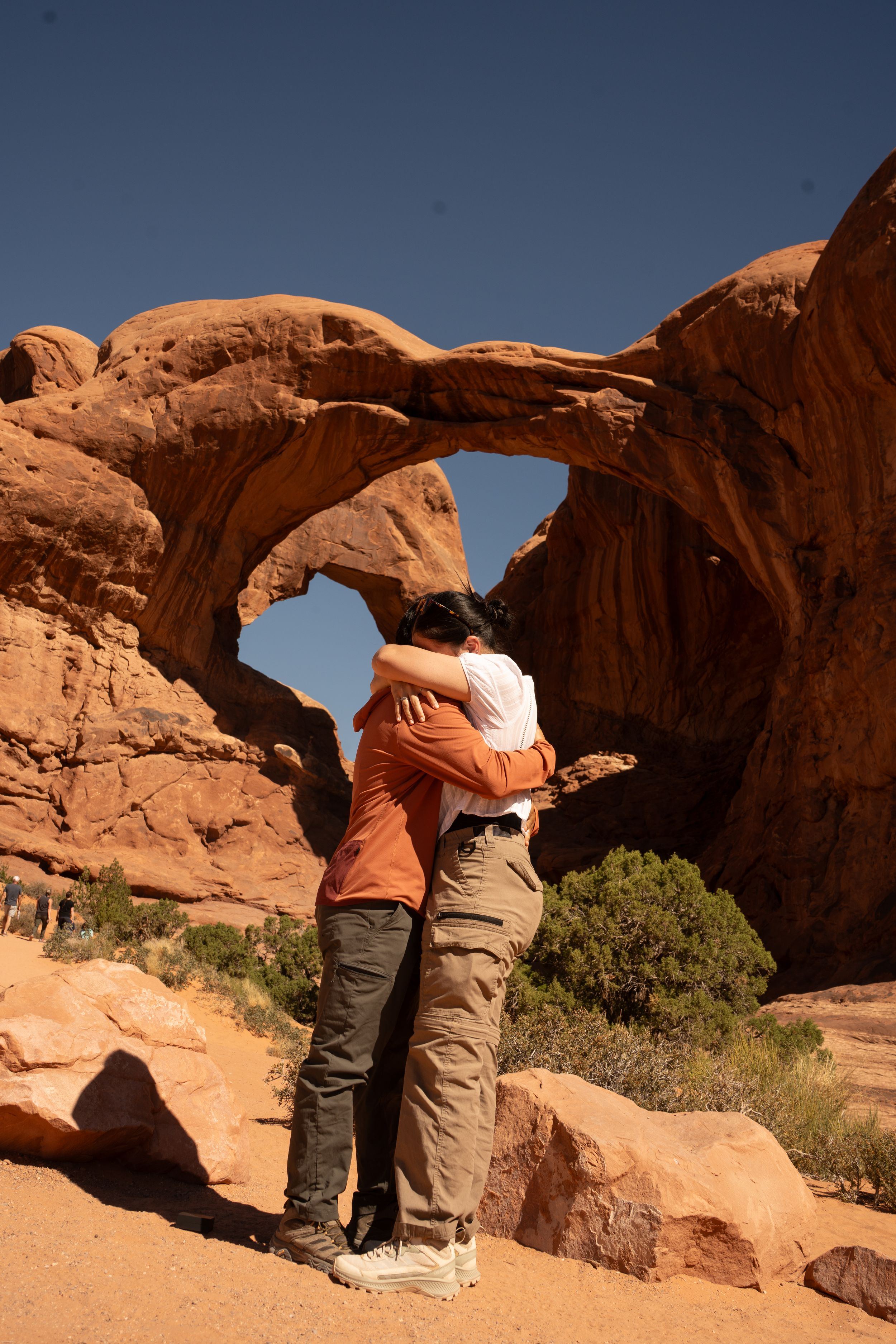 Two people embracing in front of double arches in Arches National Park, Utah.