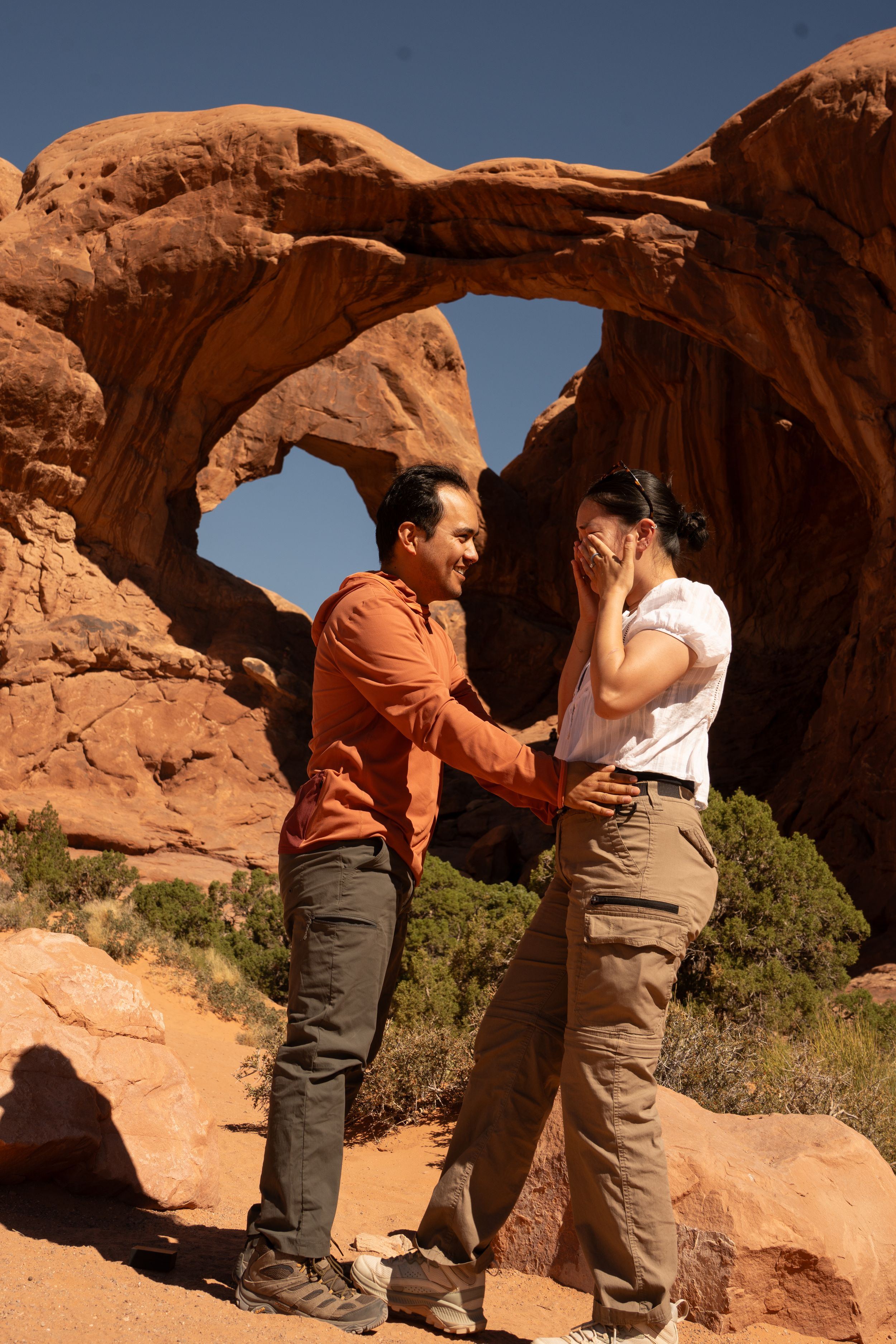Couple sharing a romantic moment at Double Arch in Arches National Park, Utah, with red rock formations.