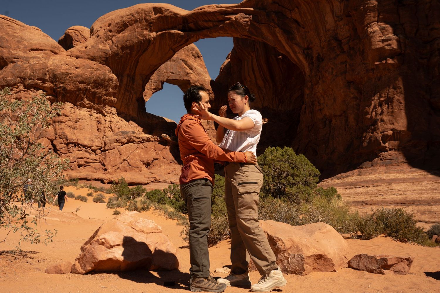 Couple embracing at Double Arch in Arches National Park, surrounded by red sandstone formations