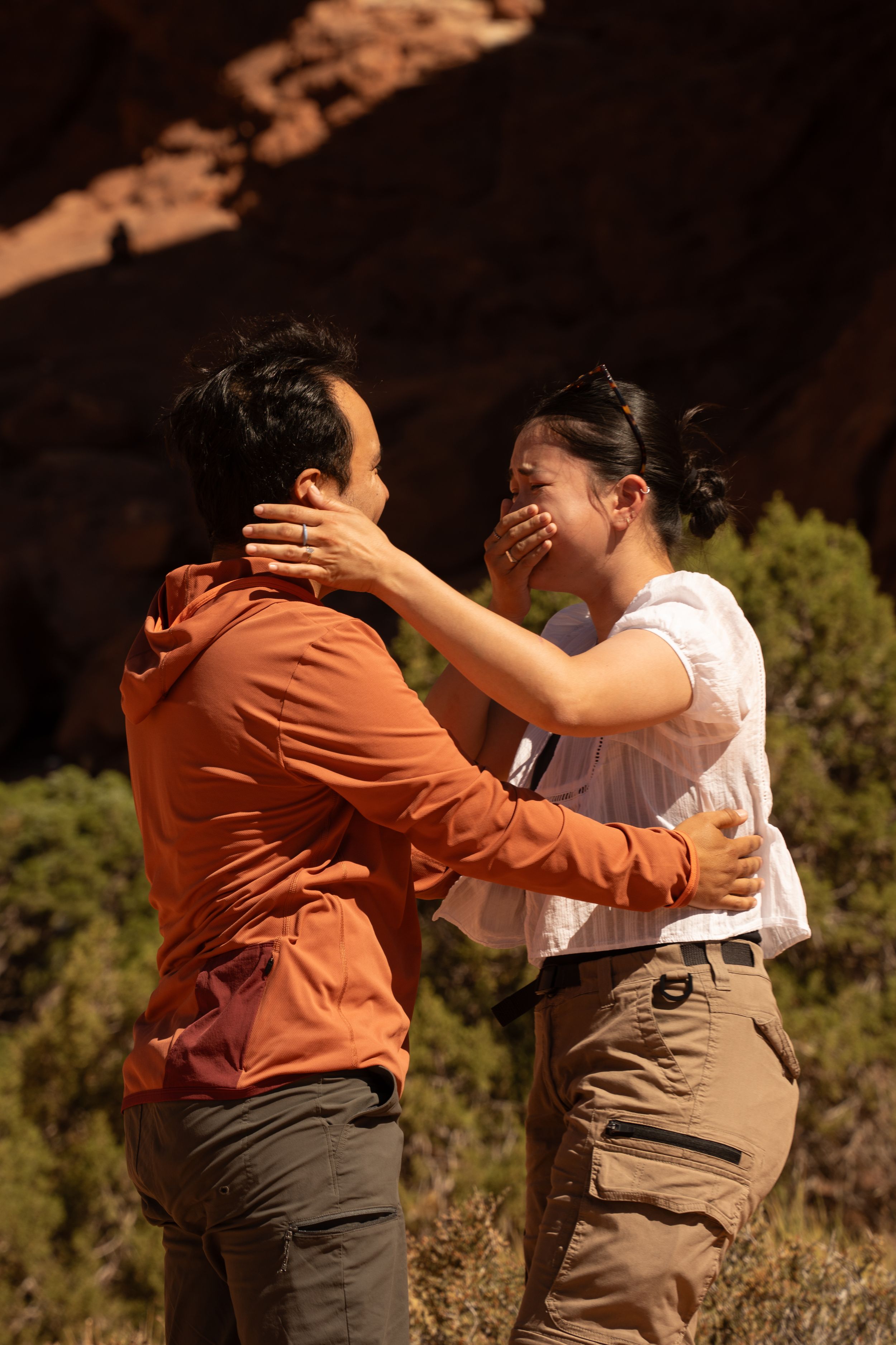 Couple sharing an emotional moment outdoors near red rock formations, woman covering her mouth in surprise.