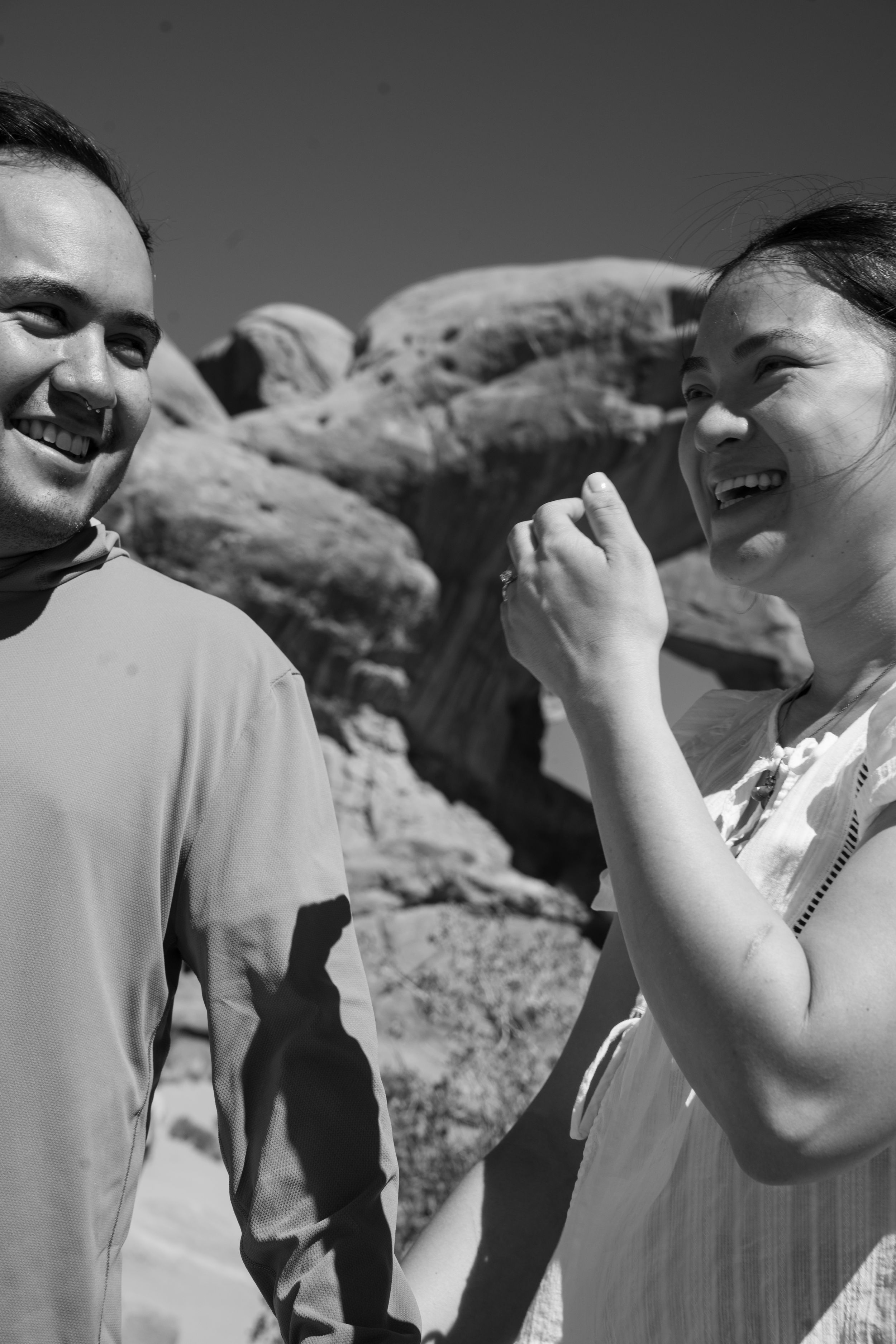 A laughing couple enjoys a sunny day outdoors with rocky desert formations in the background.