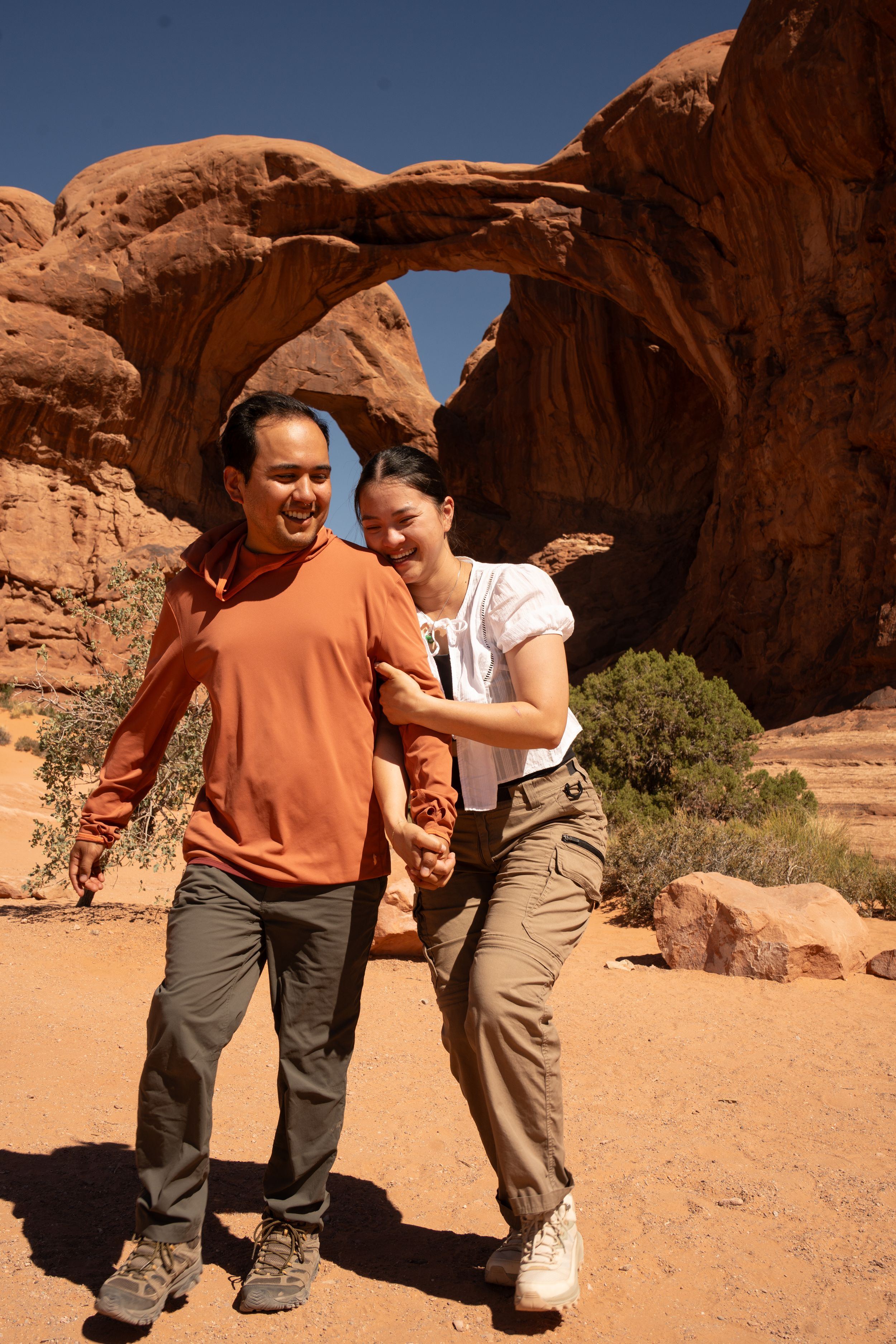 Smiling couple holding hands in front of Double Arch rock formation at Arches National Park, Utah.