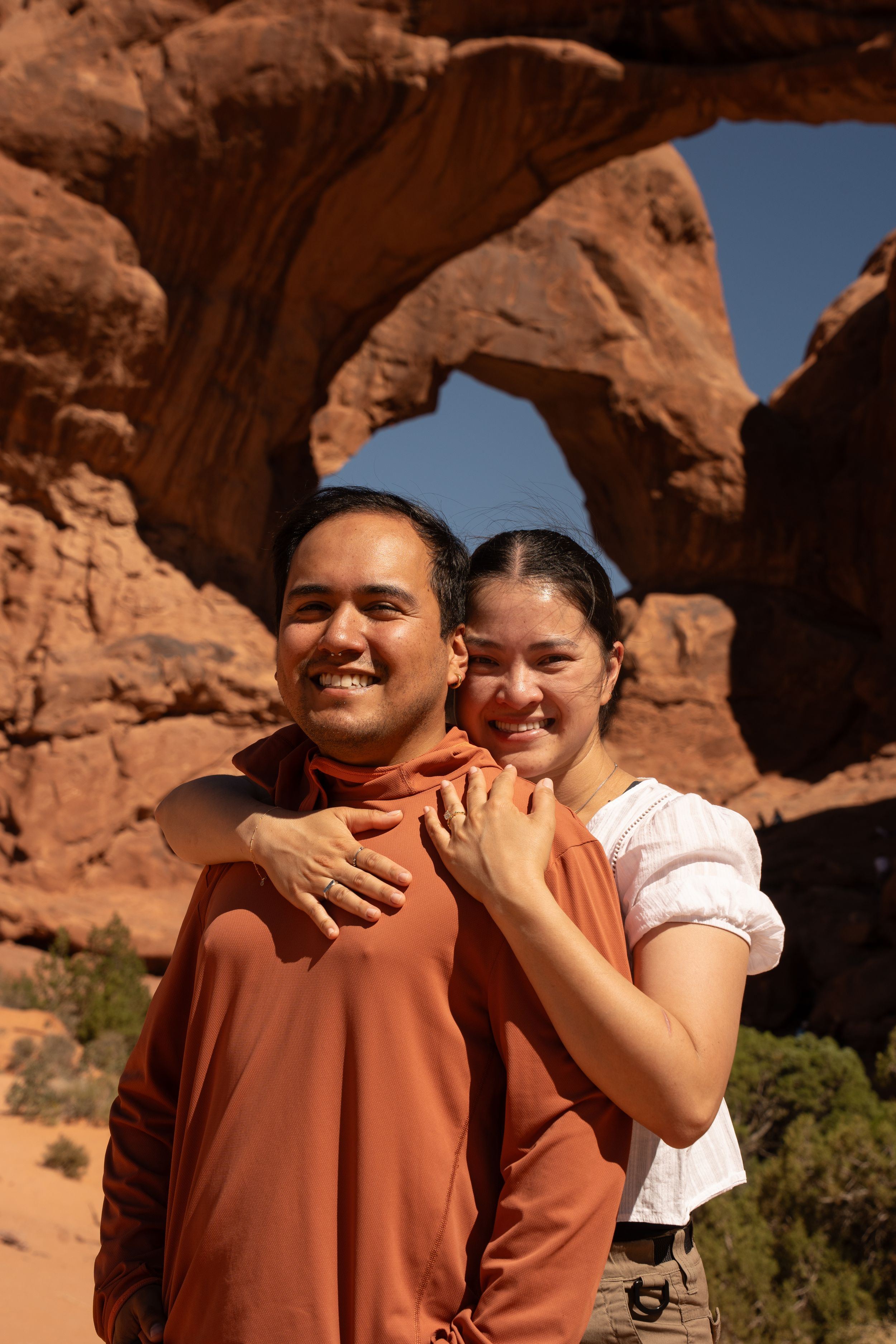 Smiling couple posing in front of a red rock arch formation at Arches National Park, Utah.