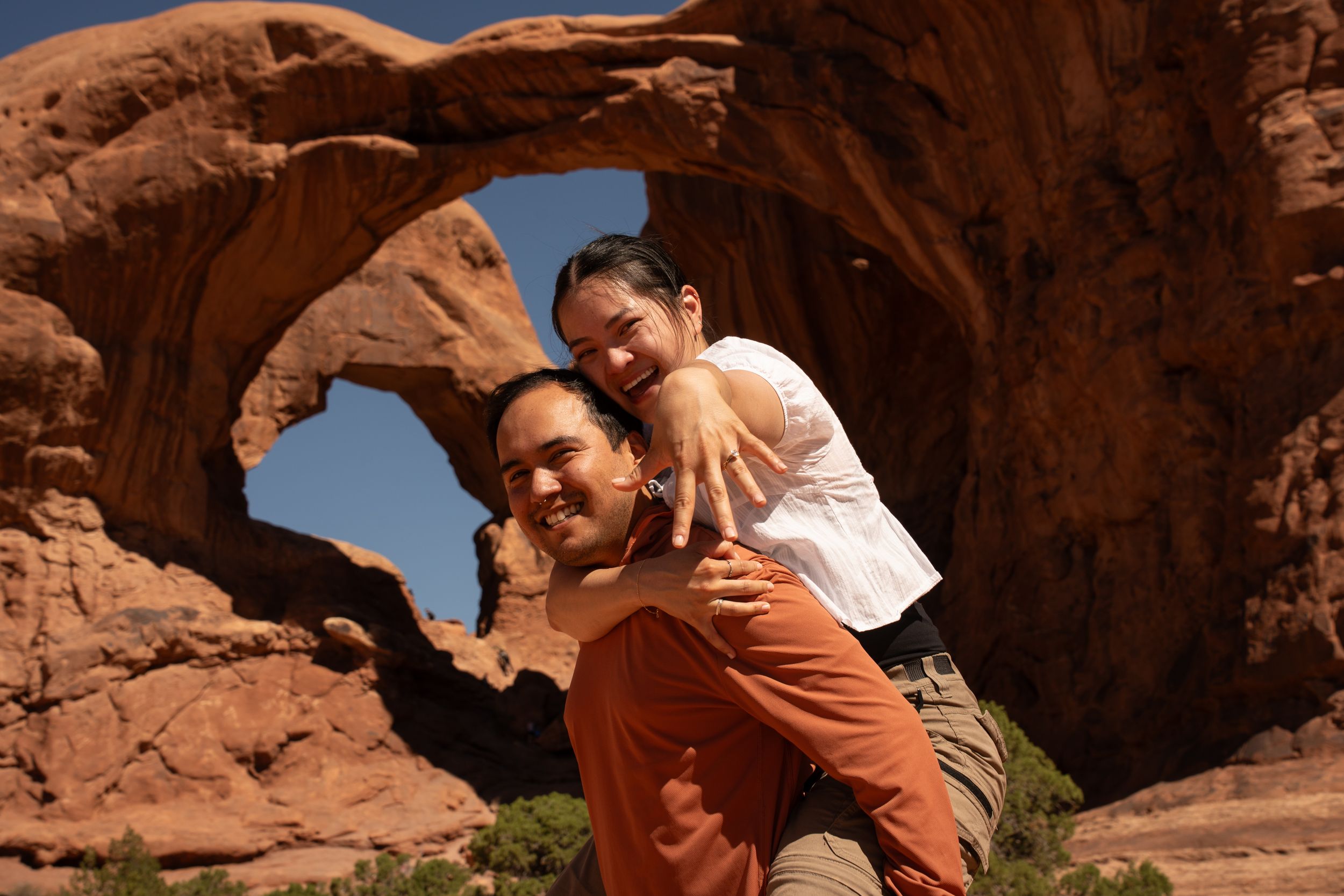 Couple posing happily in front of a natural sandstone arch at Arches National Park in Utah.