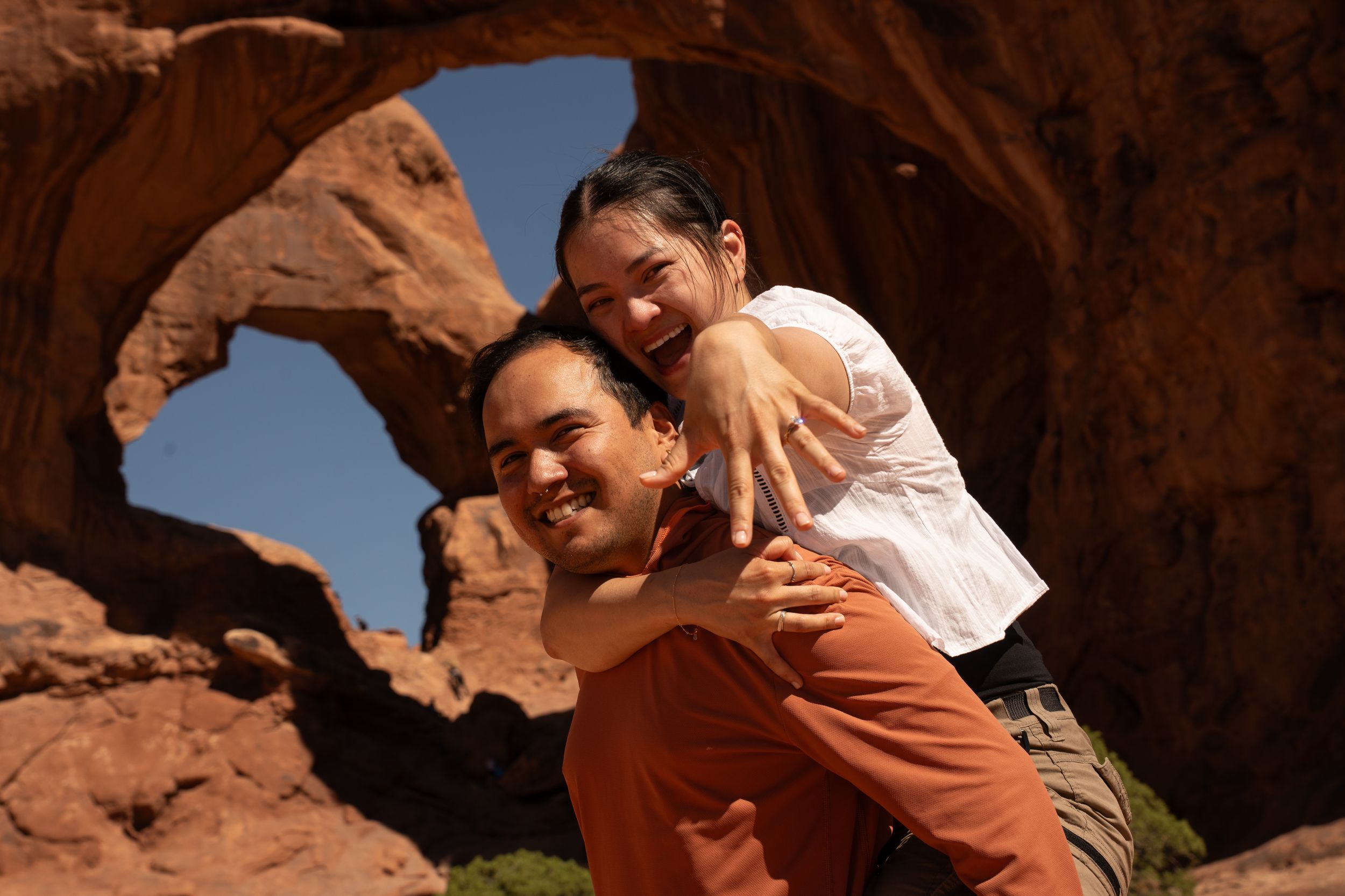 Couple posing playfully in front of a natural sandstone arch at Arches National Park on a sunny day.