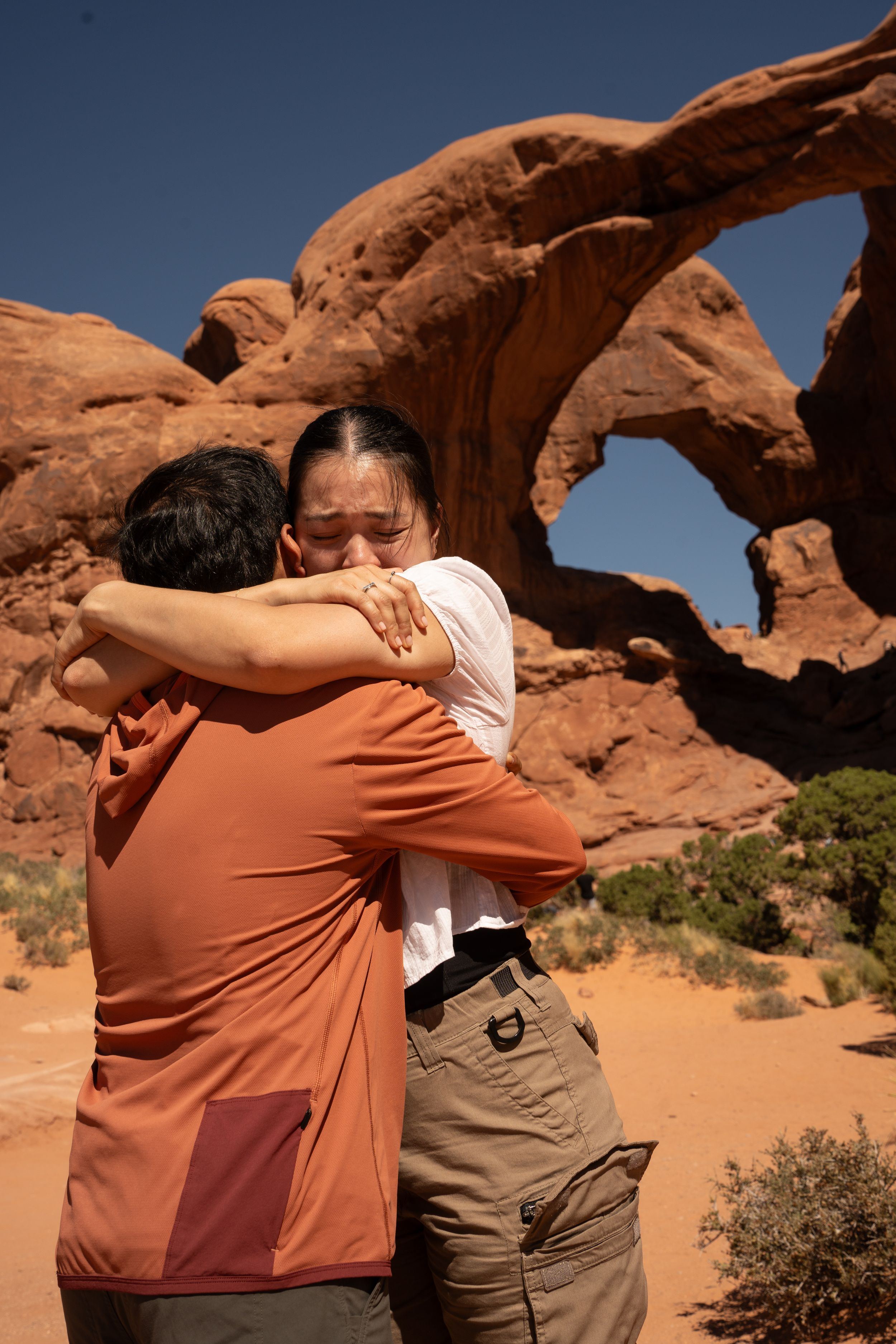 Couple embracing emotionally in front of a natural sandstone arch at Arches National Park, Utah.