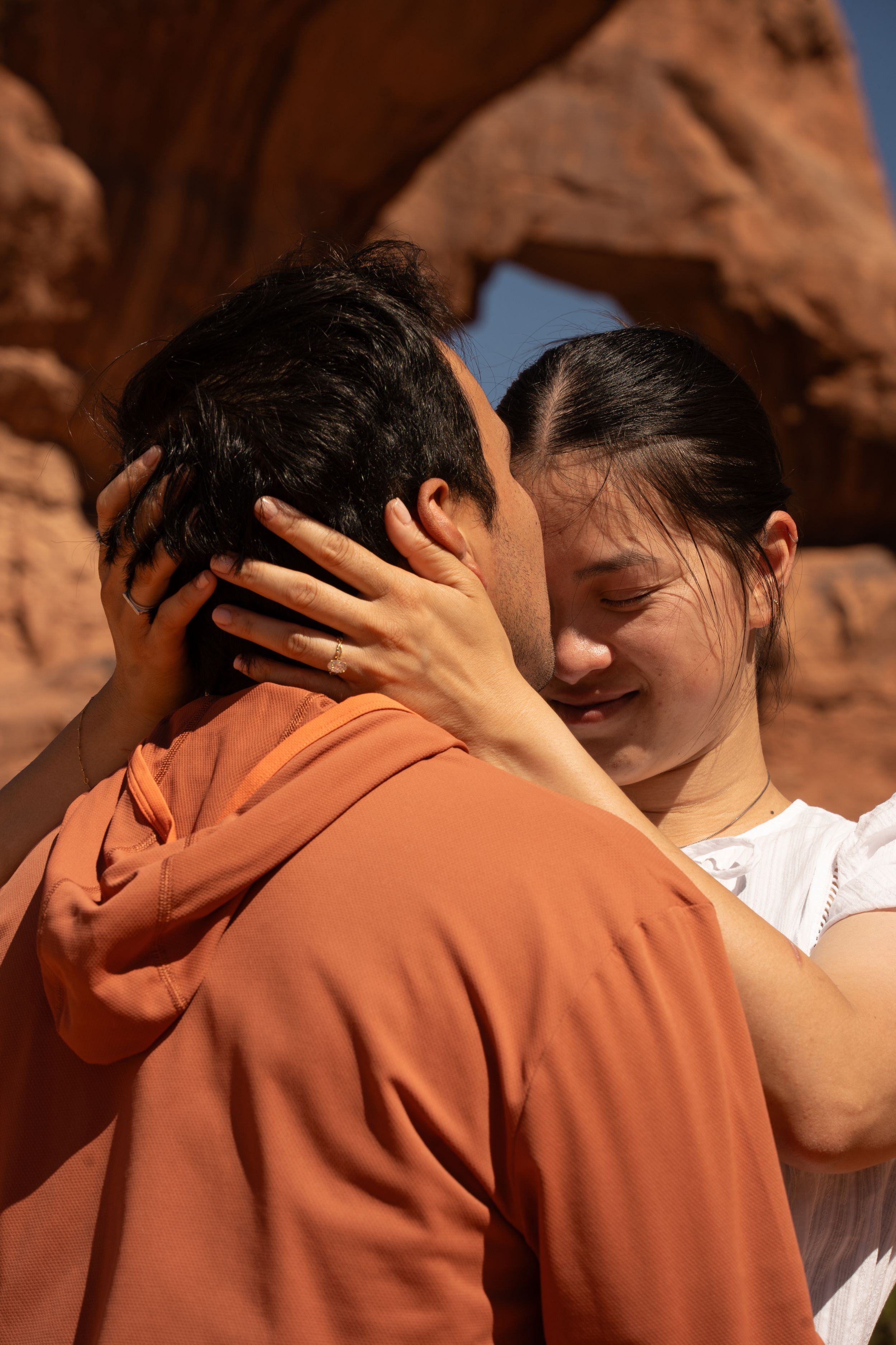 Couple sharing a romantic kiss in front of red rock formations at Arches National Park.