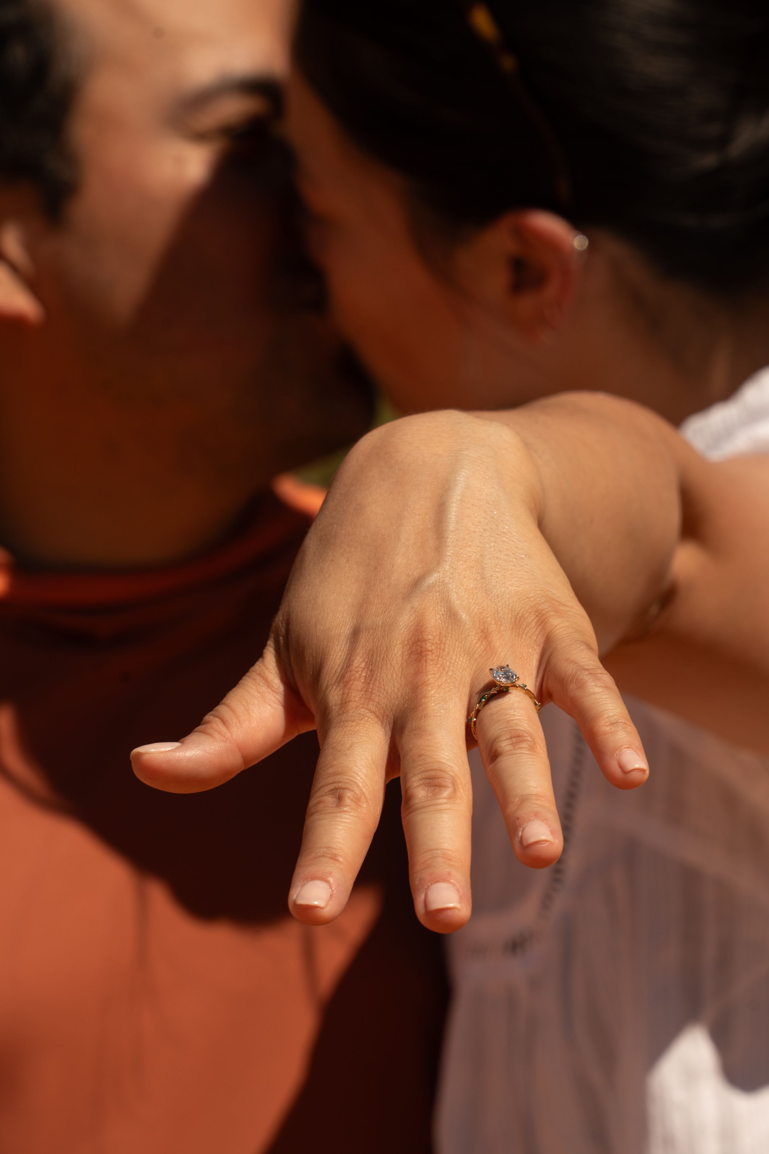 Couple sharing a kiss while showing off an engagement ring with a green gemstone stone on her finger.