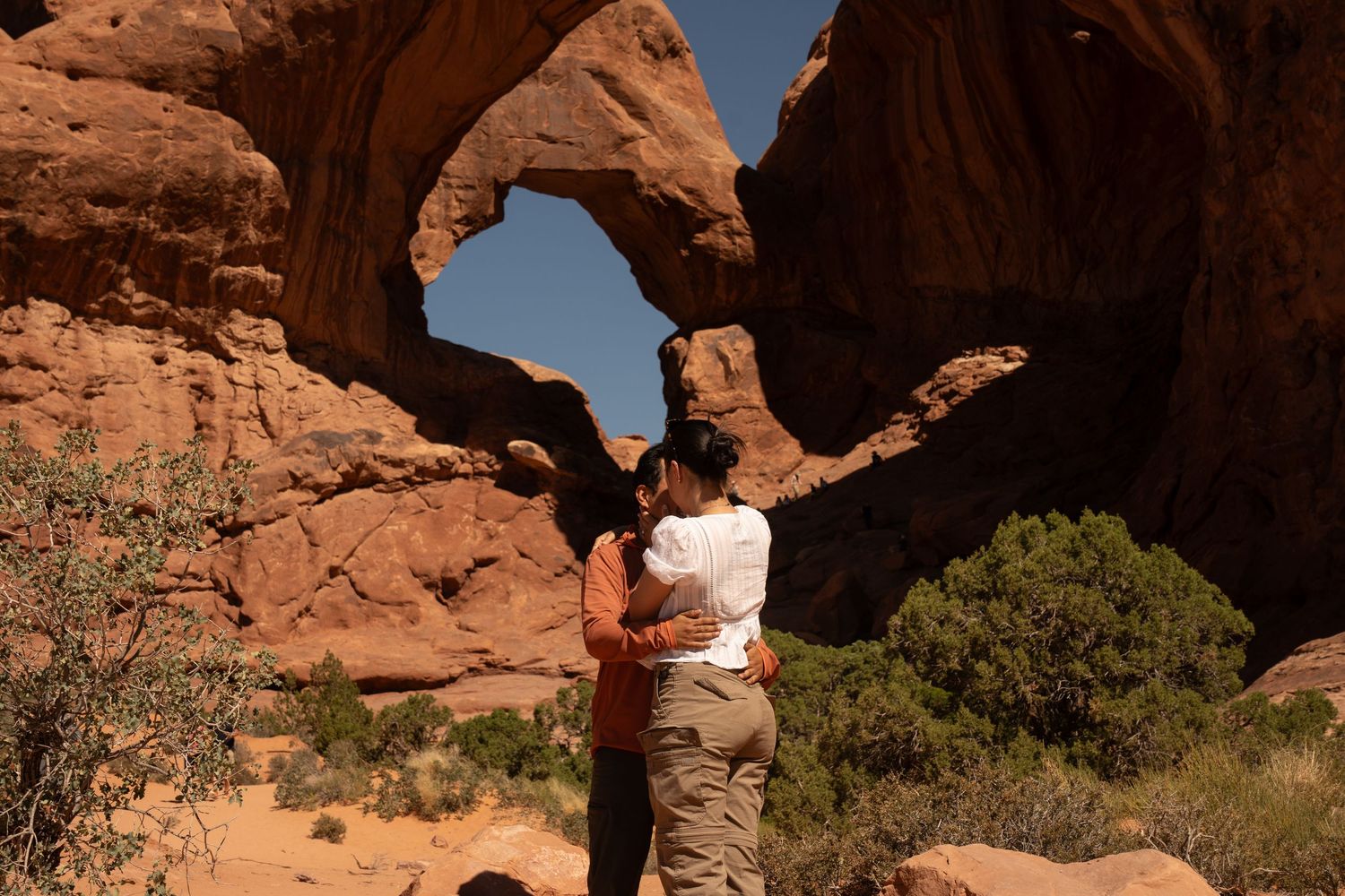 Couple embracing before Double Arch in Arches National Park, Utah, on a sunny day