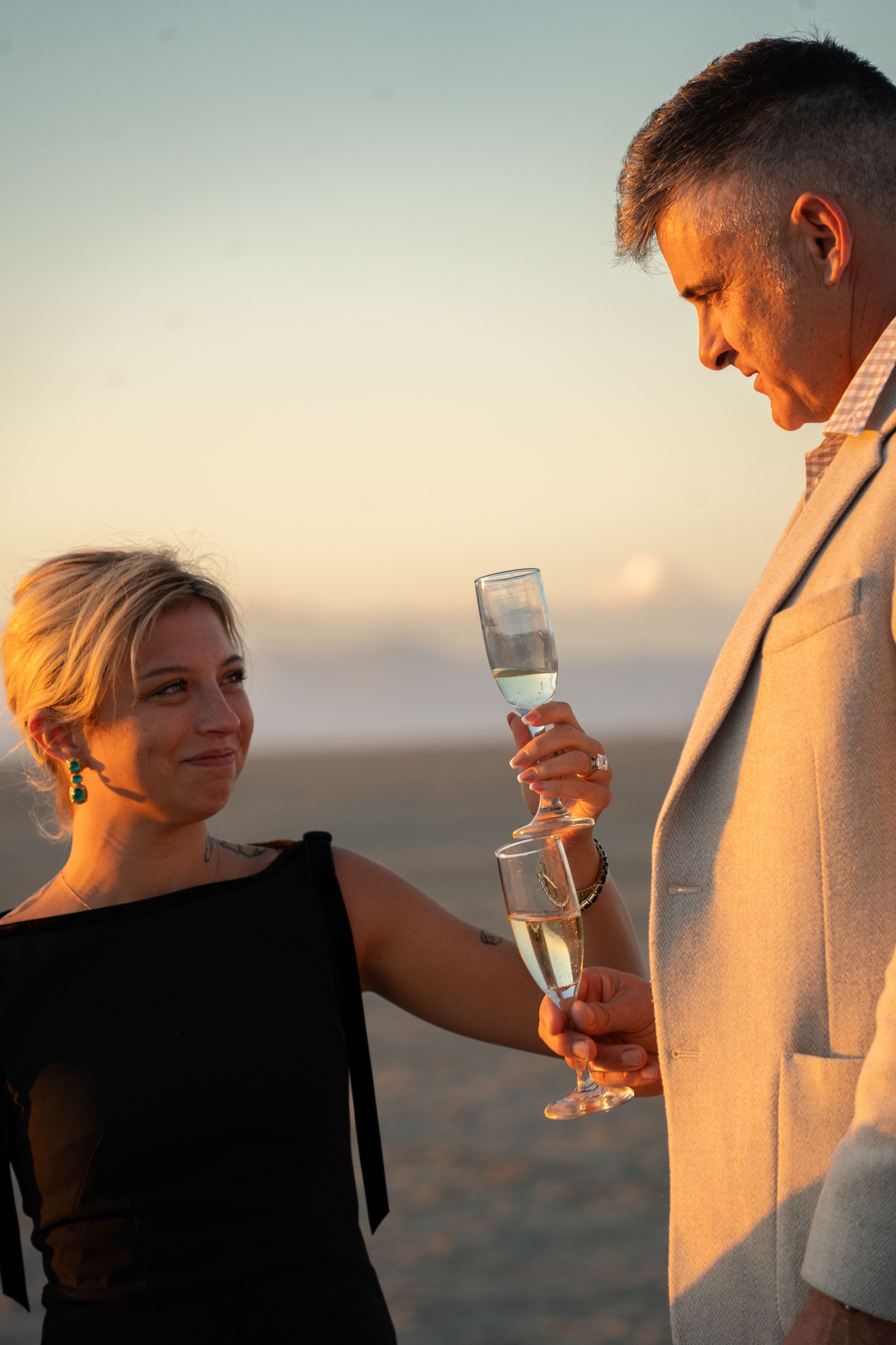 couple raises champagne glasses to celebrate proposal at the salt flats of the great saltair