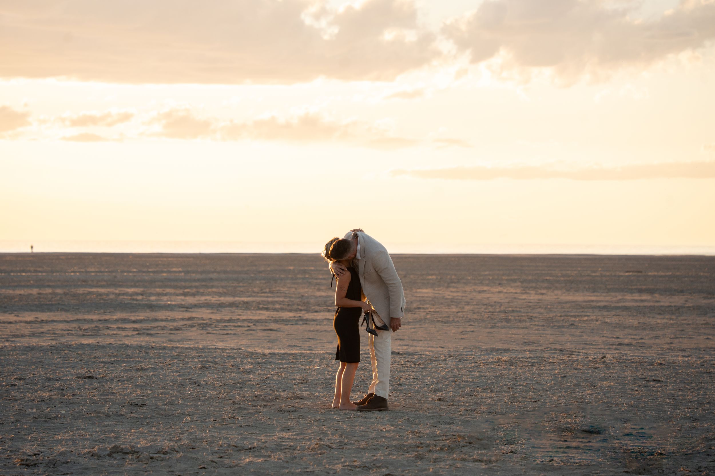 Couple sharing a romantic kiss at sunset on a vast open desert plain with golden sky.