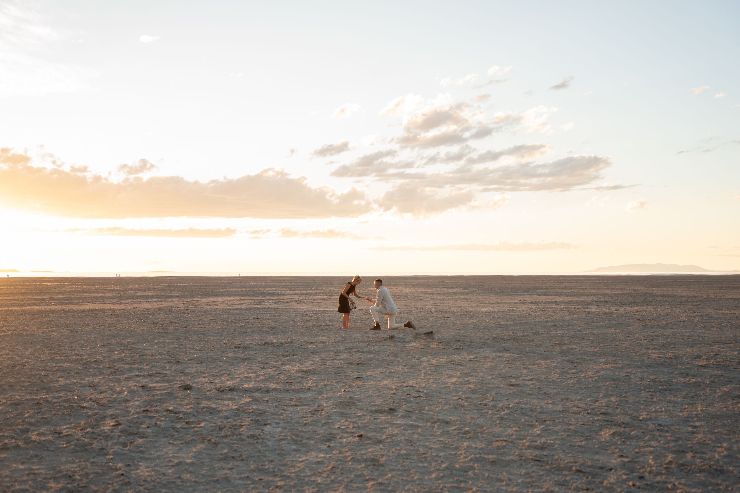 man proposing on vast salt flats at golden sunset, wide open landscape with soft clouds.