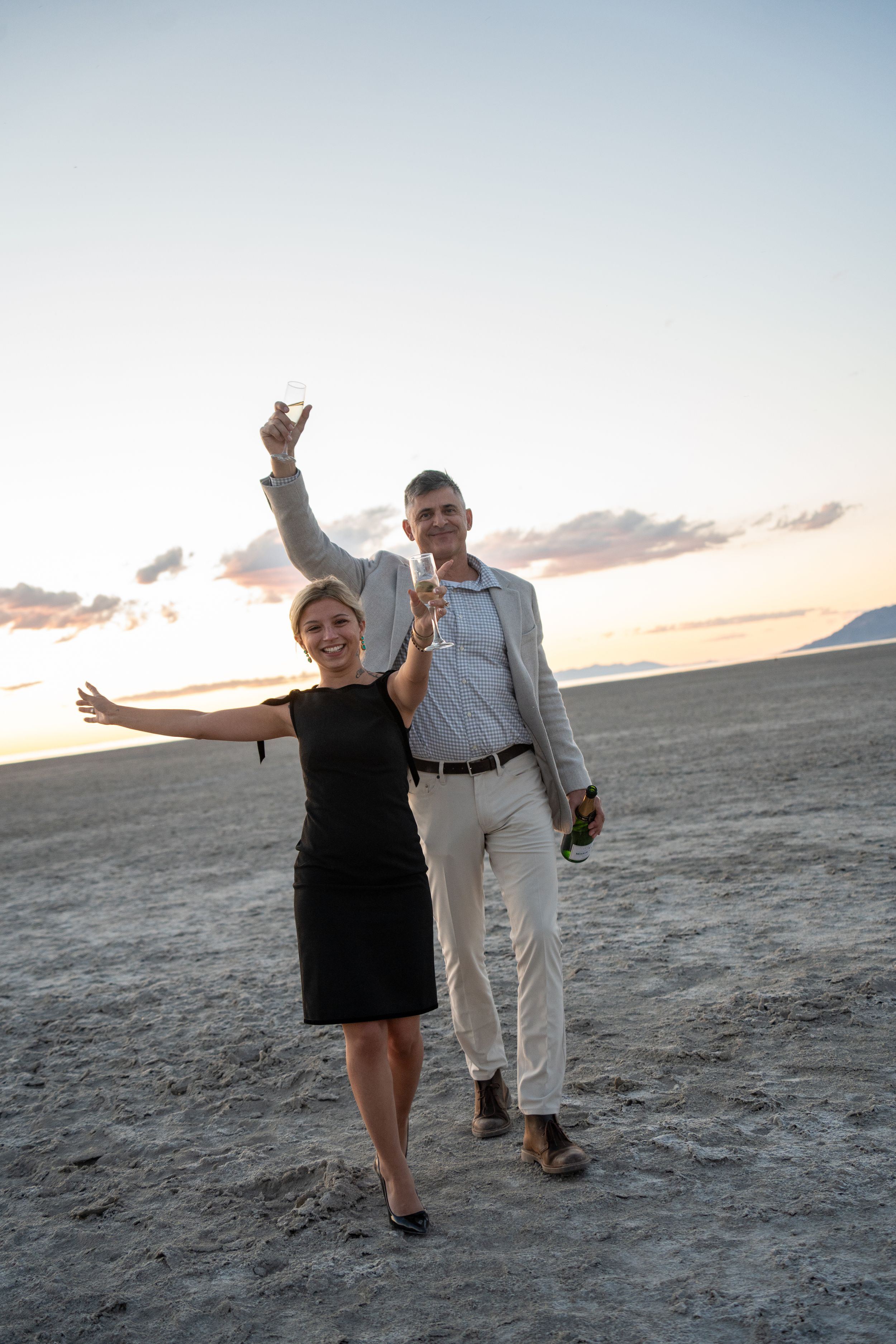 couple walking and raising champagne glasses to celebrate their engagement at the great saltair