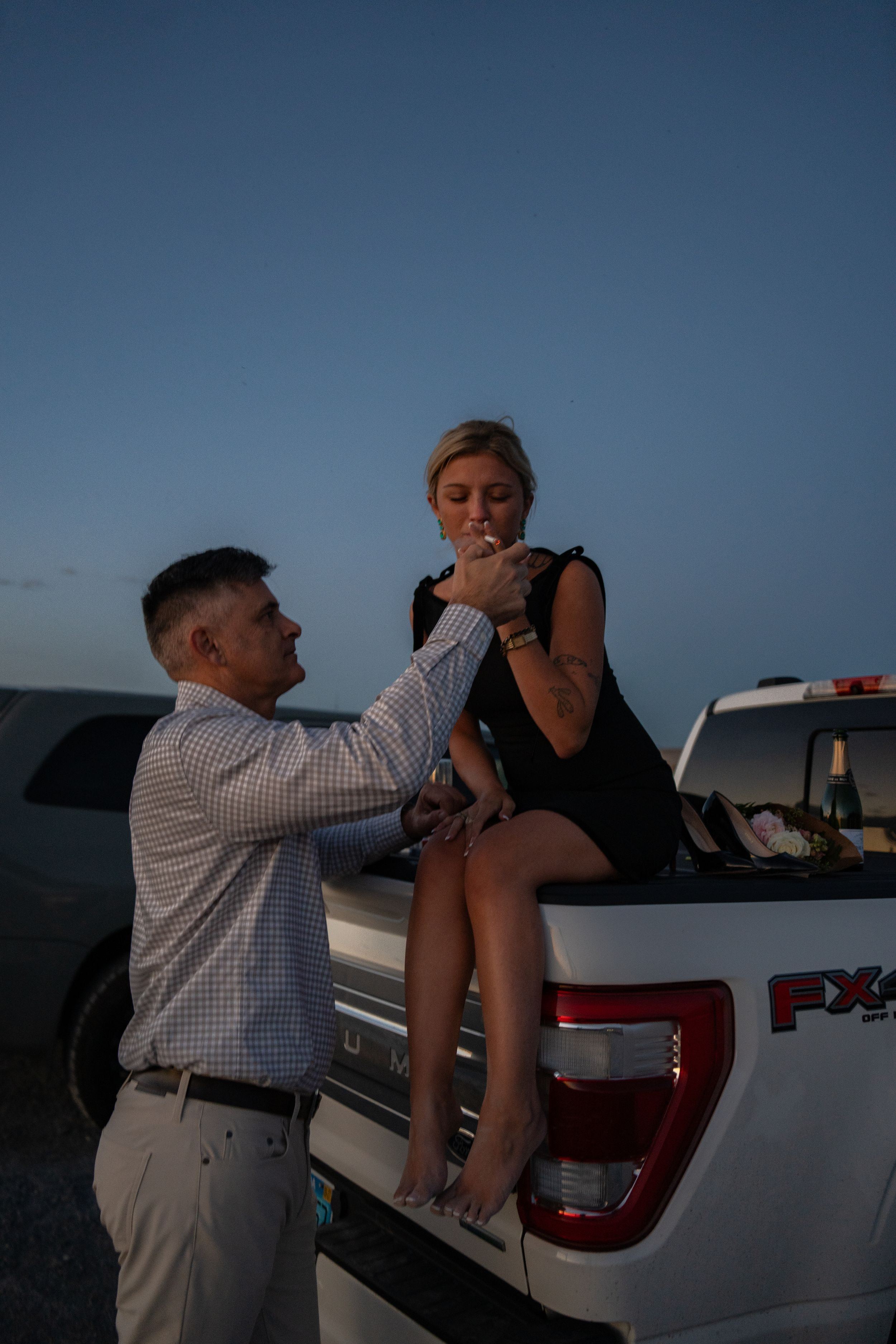 Man proposing to woman sitting on Ford FX4 truck tailgate at dusk outdoors.