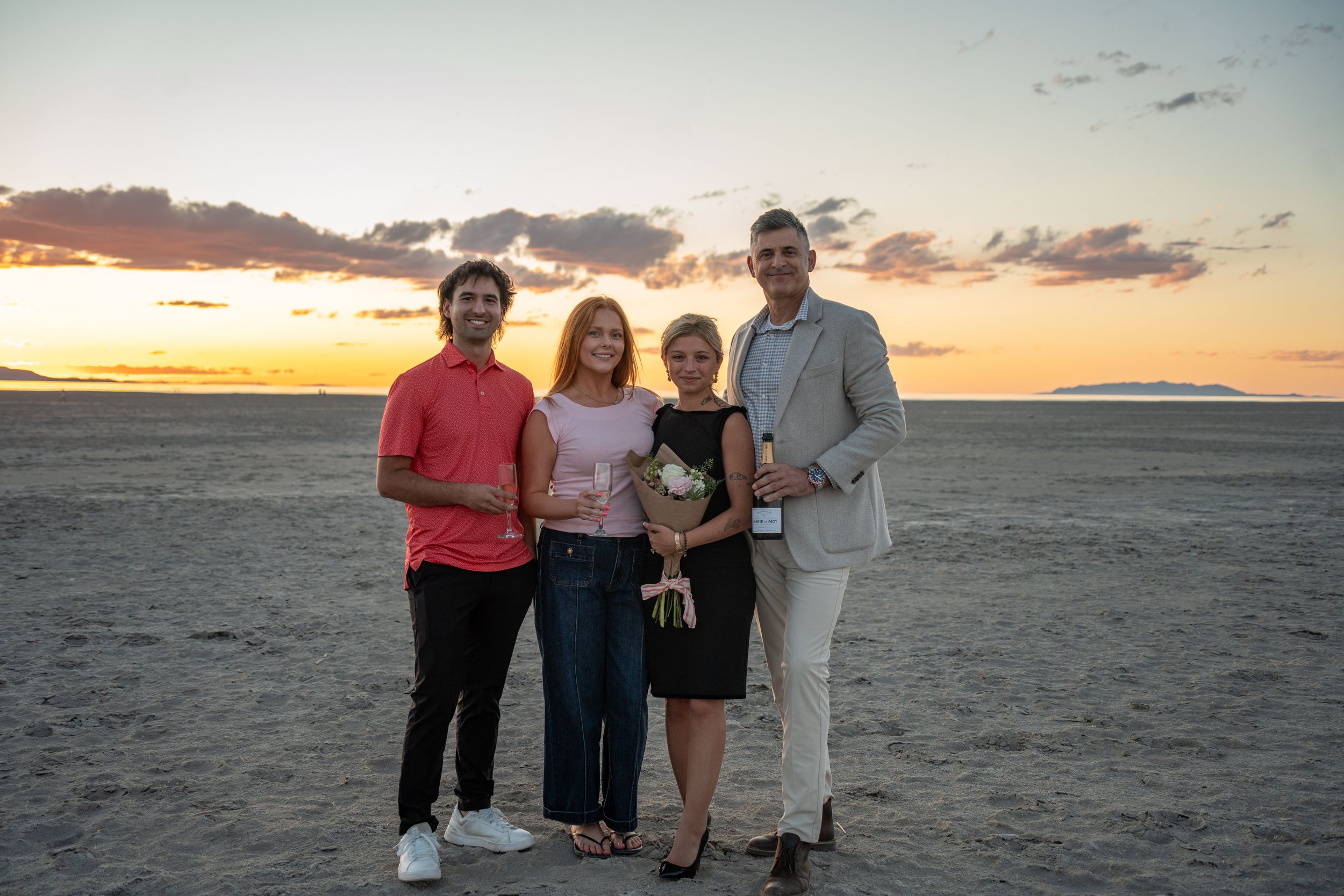 couple poses with their friends who helped with their proposal on salt flats of great saltair with champagne and flowers