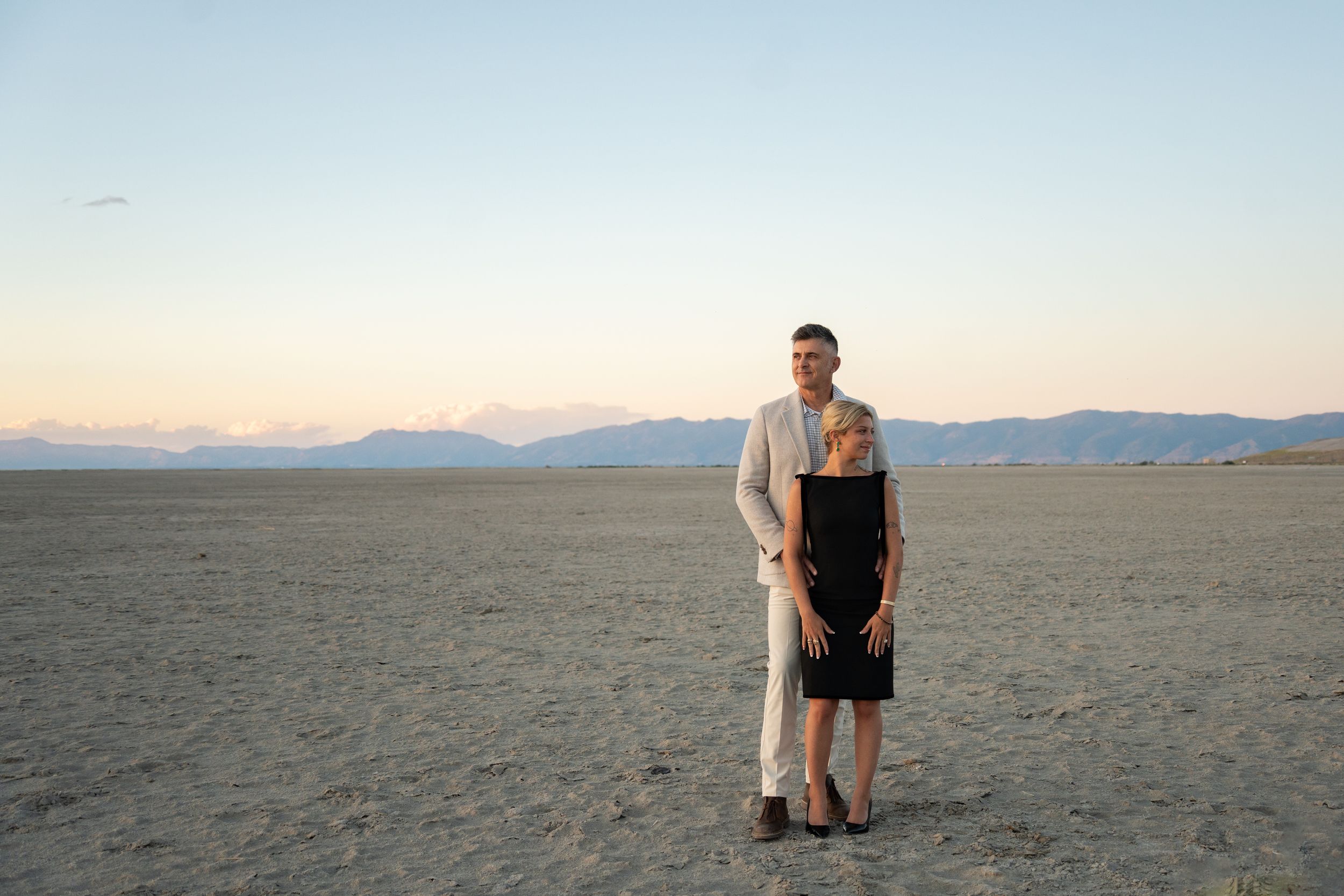 couple standing embracing each other on salt flats with wasatch front in the background after personal engagement