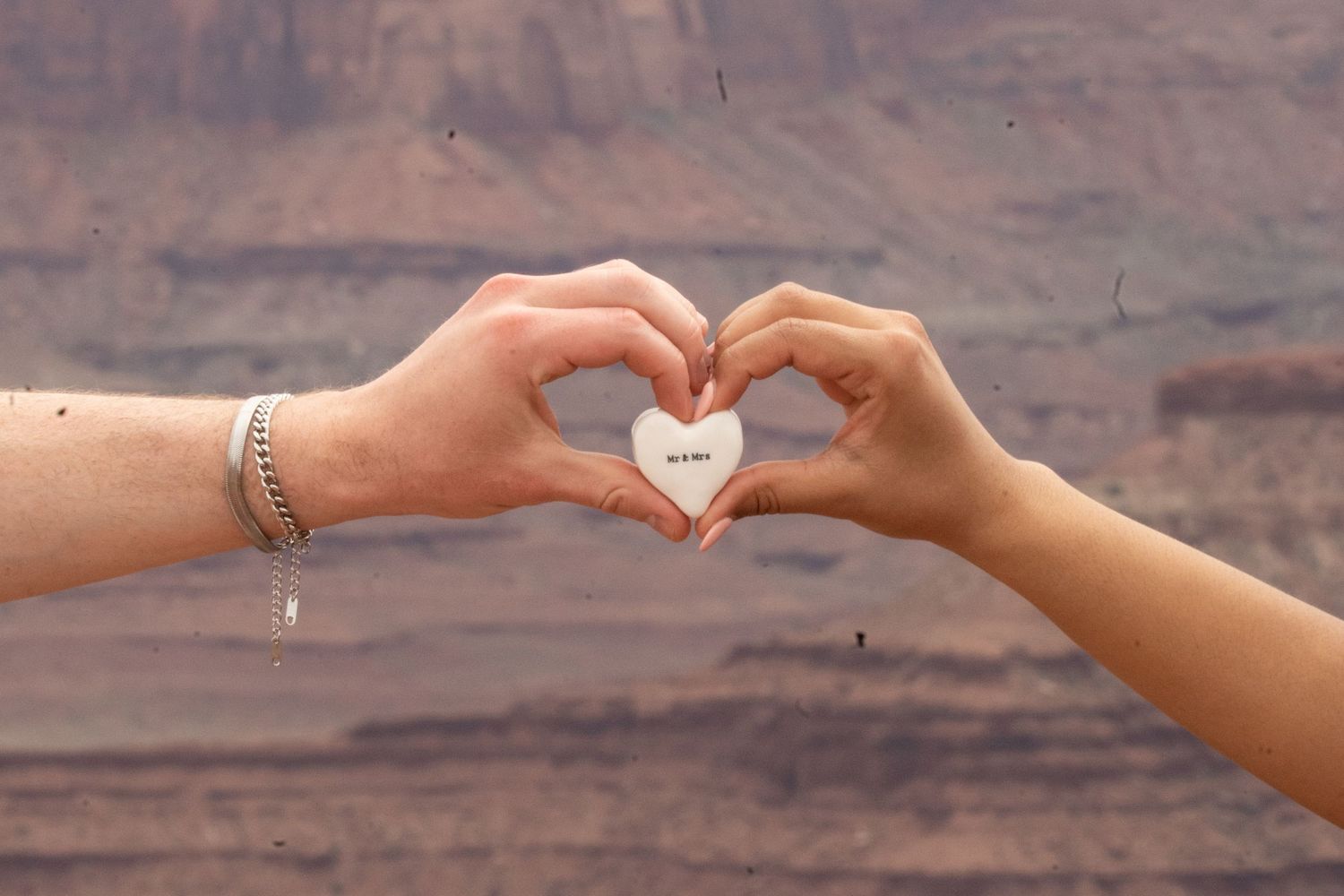 Two hands forming a heart shape holding a small white heart stone with dead horse point canyon landscape in the background.