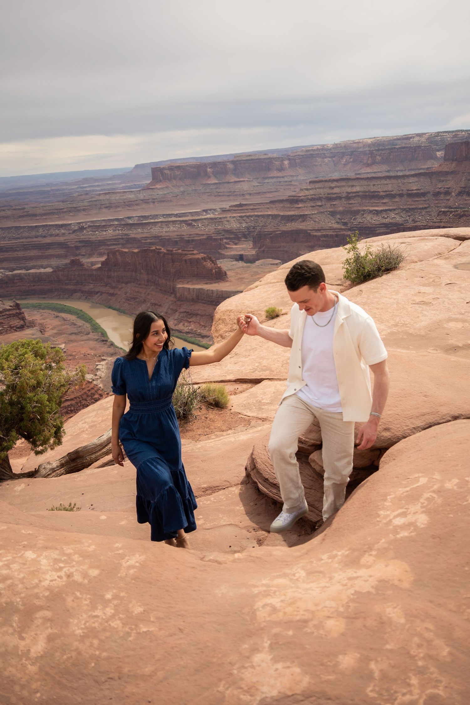 Couple holding hands on red rock canyon overlook above Canyonlands, Colorado River visible far below
